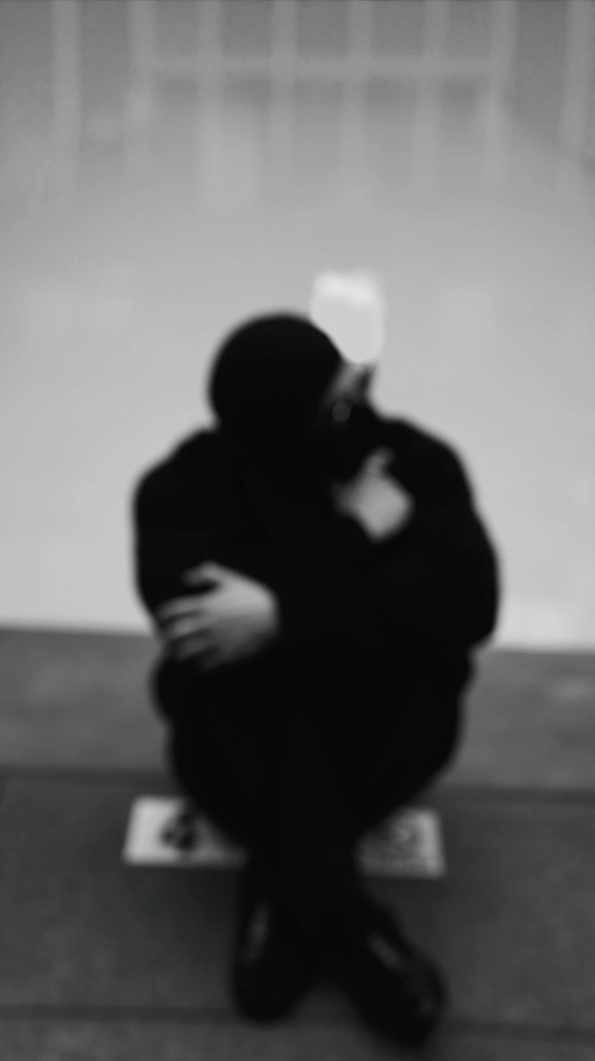 A person in a black hoodie taking a photo of their reflection in a mirror with a smartphone, standing in a room with minimal decor.