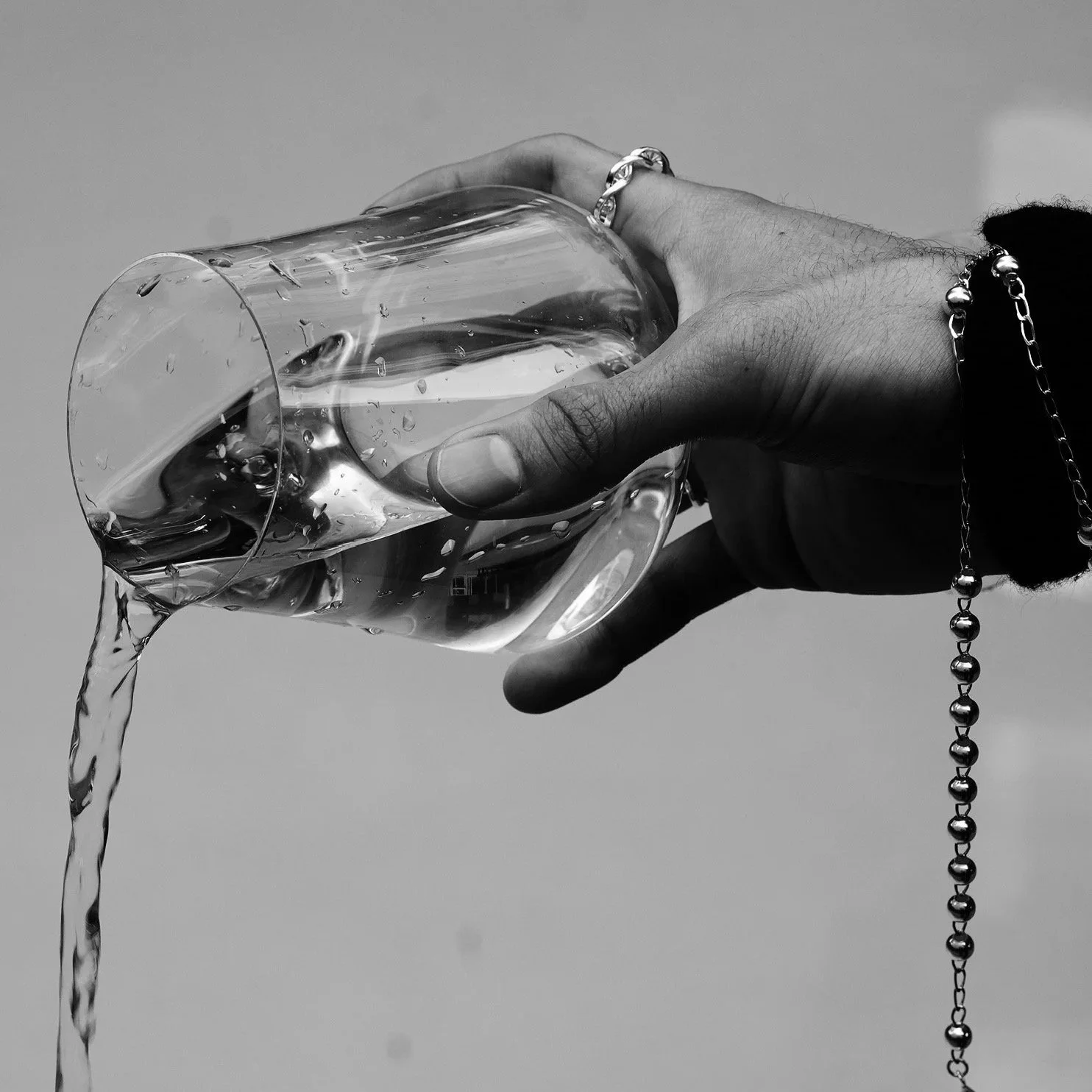 A hand holding a glass of water, with water spilling out, against a plain background.