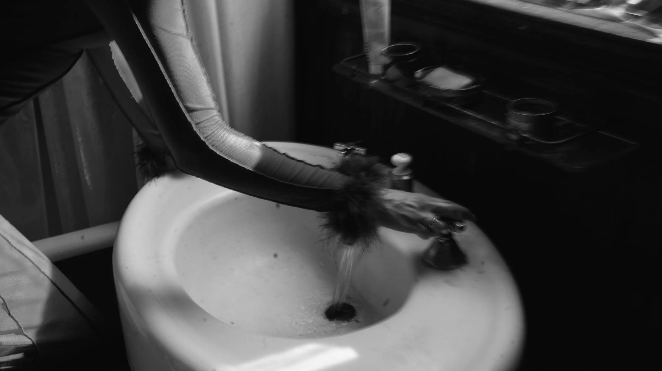 A black and white photo of a dog drinking water from a sink with a flexible hose in a kitchen.