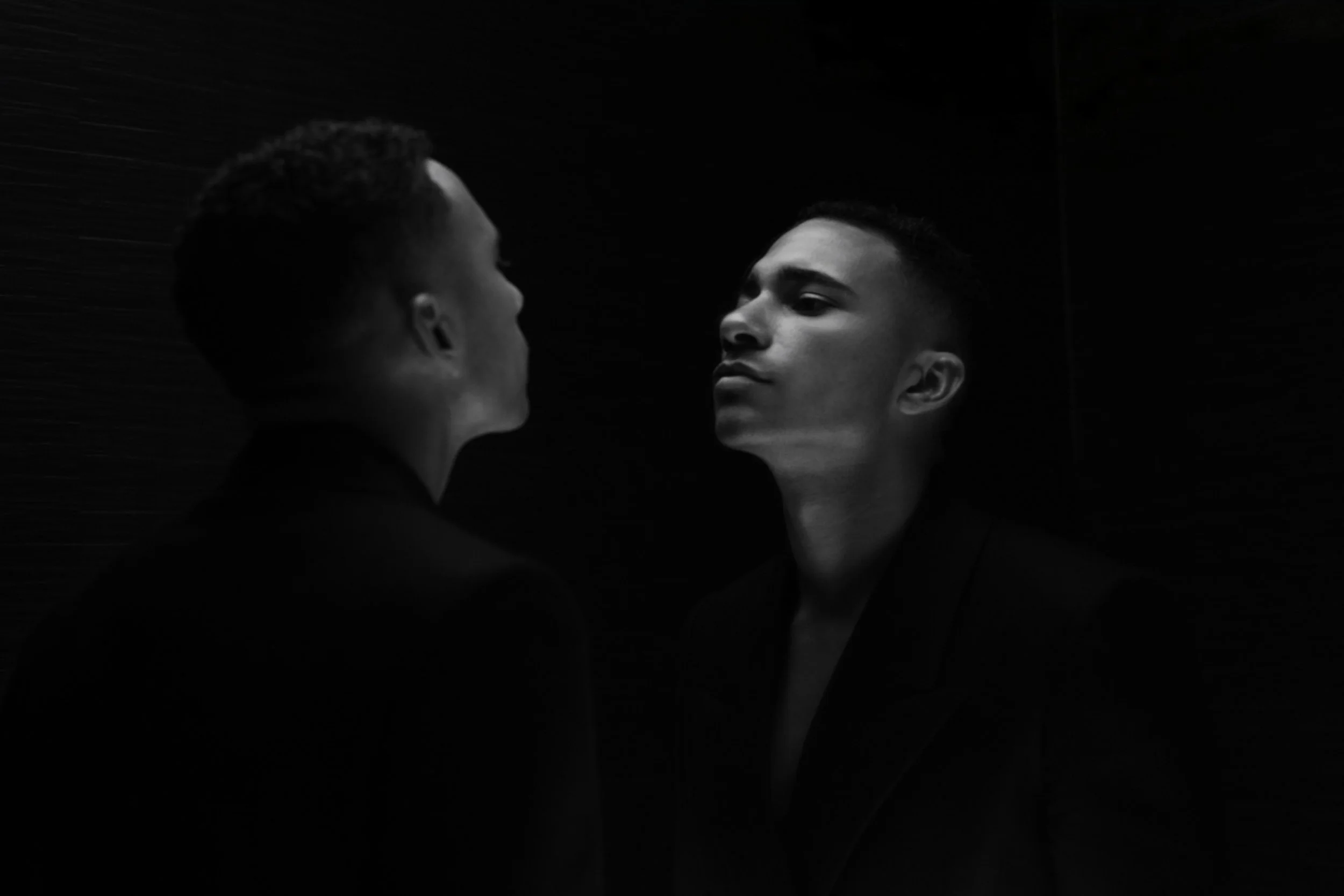 Two young men facing each other closely in a dimly lit environment, black and white photograph.