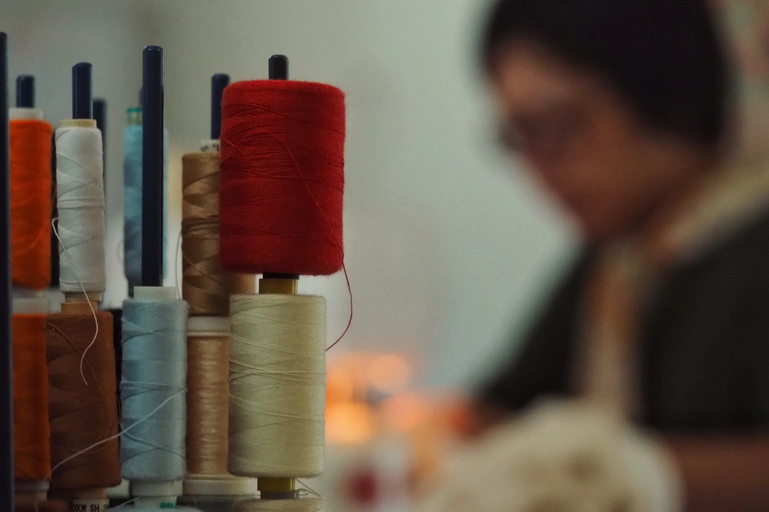 Various spools of thread in different colors including orange, white, beige, cream, and red, arranged vertically with a blurred background.