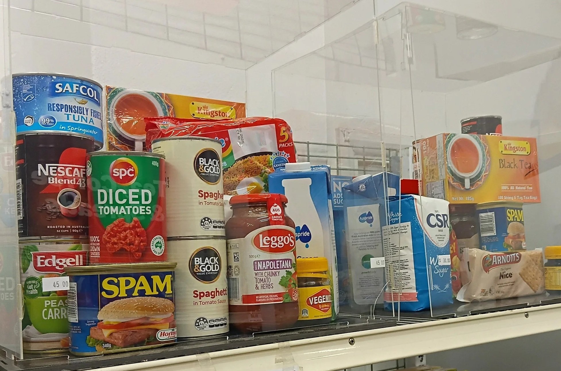 A store shelf stocked with canned and packaged food items, including tuna, diced tomatoes, spaghetti, spam, and other pantry staples.