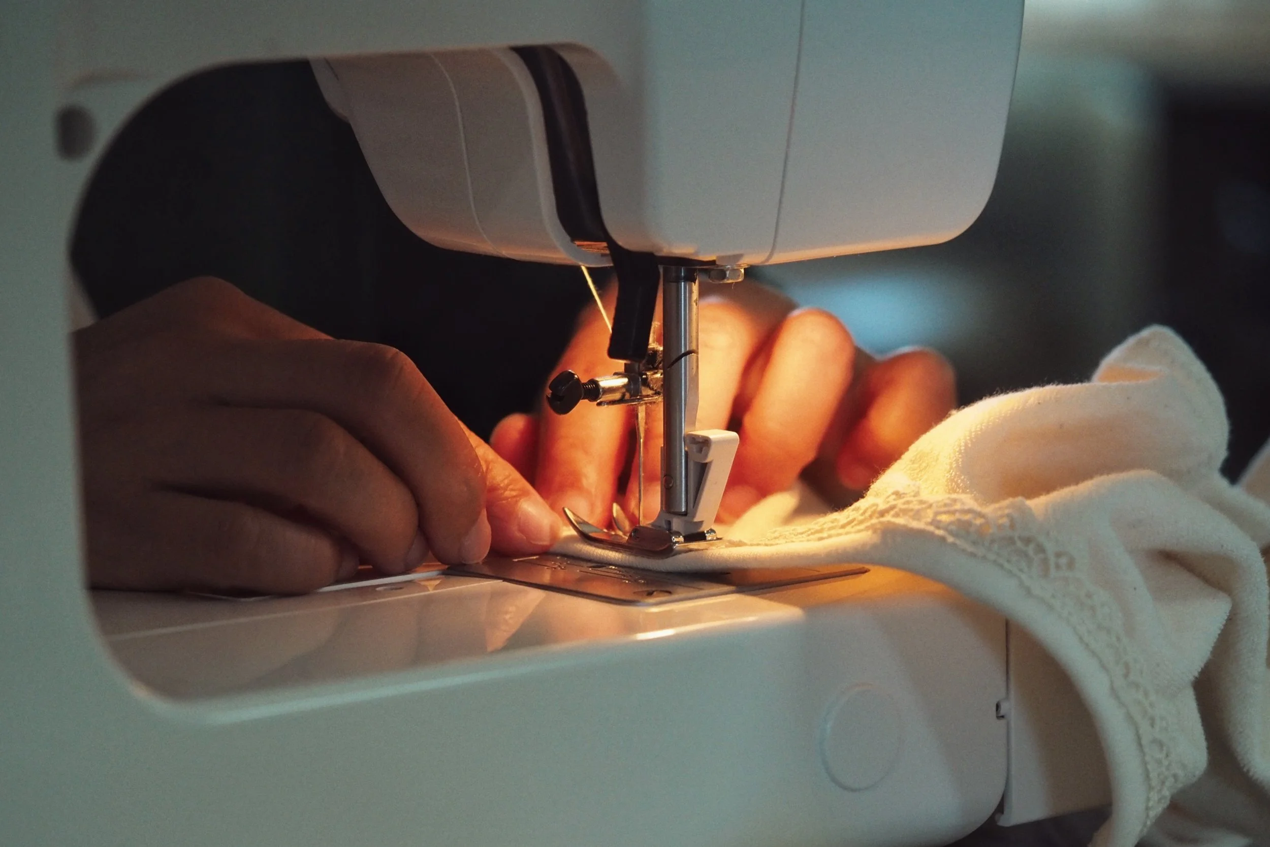 Close-up of a sewing machine stitching fabric with hands guiding the cloth.