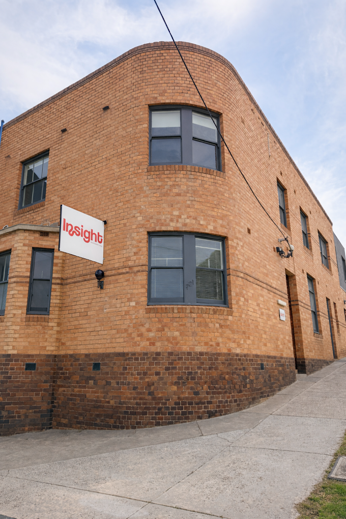 Red brick building with black-framed windows, a white sign that reads 'Insight', and a sidewalk in front.