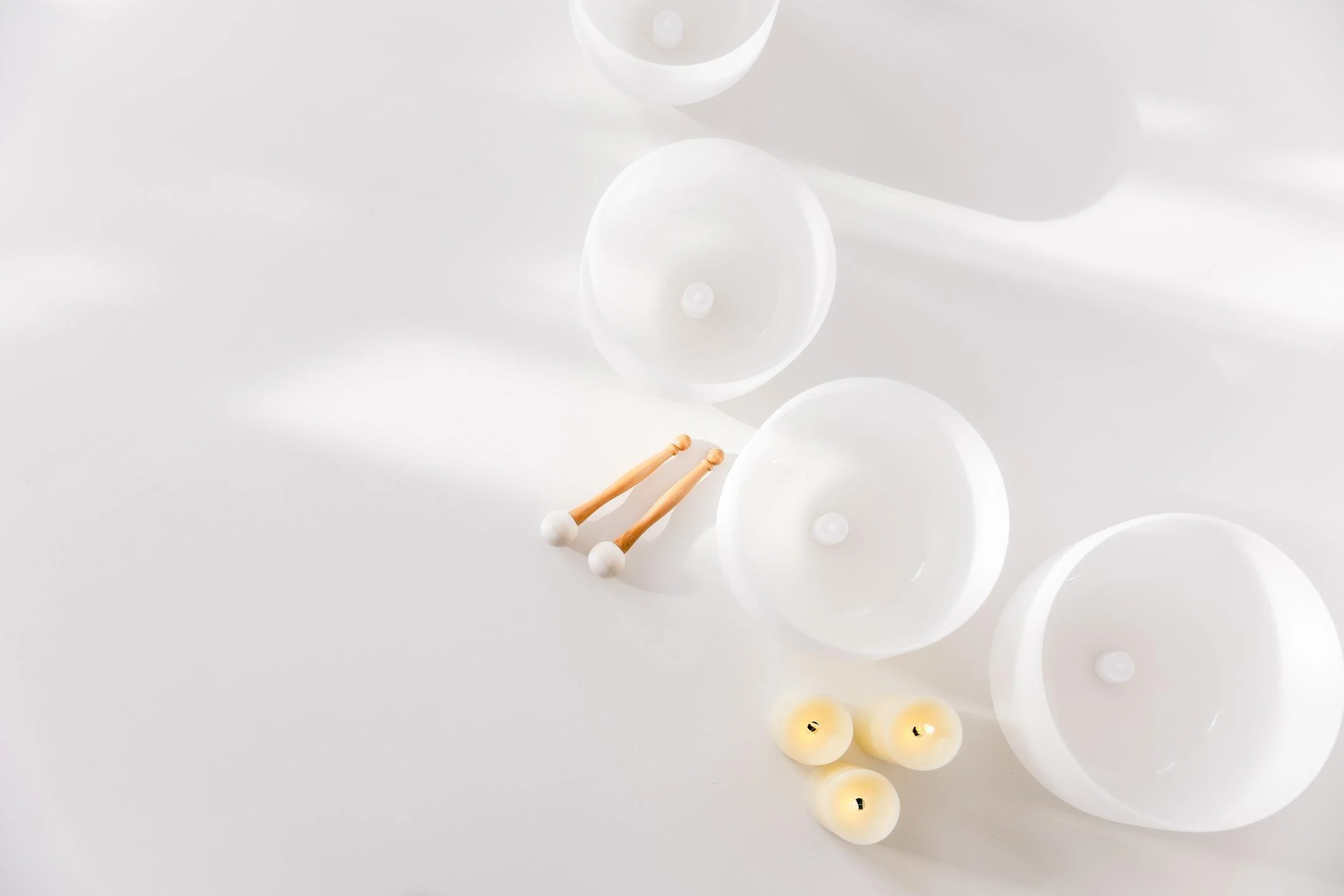White balloons of various sizes, three lit candles, and two small wooden mallets with white balls on the ends, arranged on a white surface.