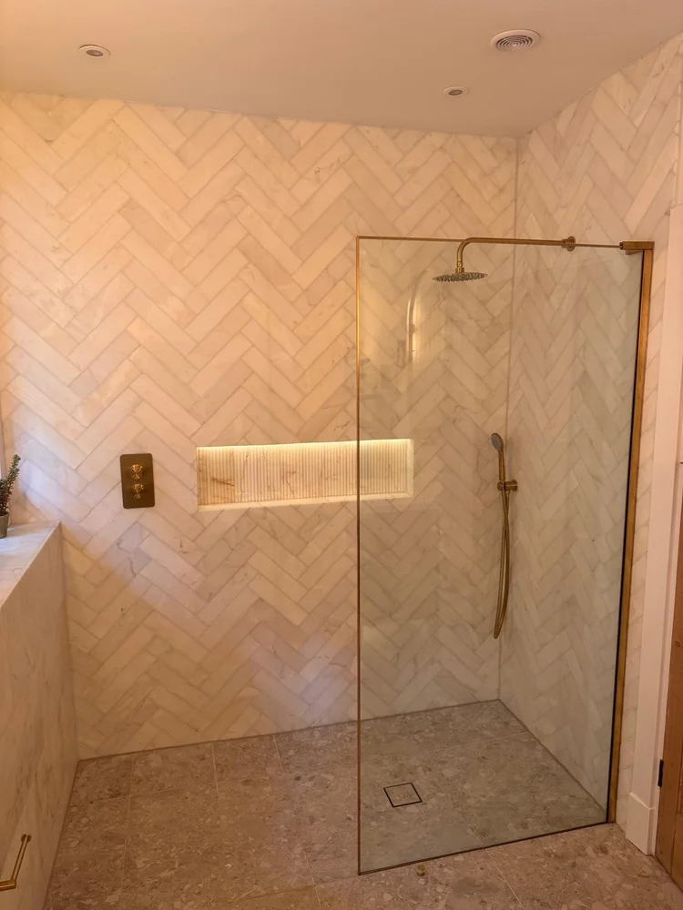 Marble herringbone tiled walk-in shower with gold fittings and illuminated niche — bathroom installation Nottingham