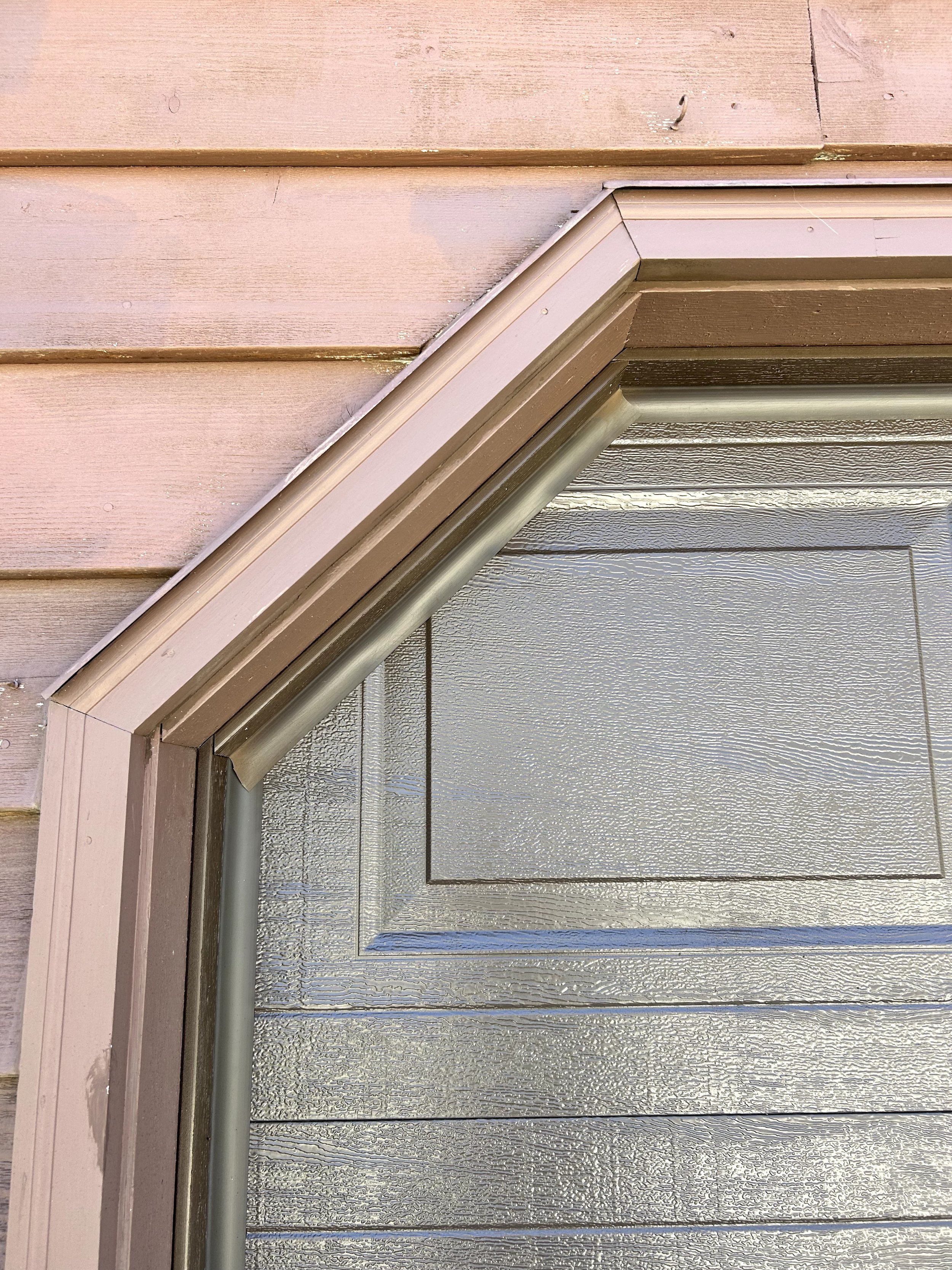 Close-up view of a house siding with pink and silver-colored horizontal panels, decorative trim, and a downspout pipe.