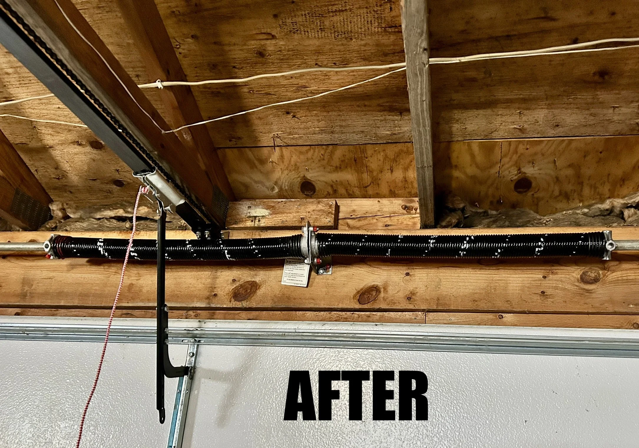 Garage ceiling with wooden beams, electrical wiring, and a garage door opener installation, with part of a sign visible that says 'AFTER'.