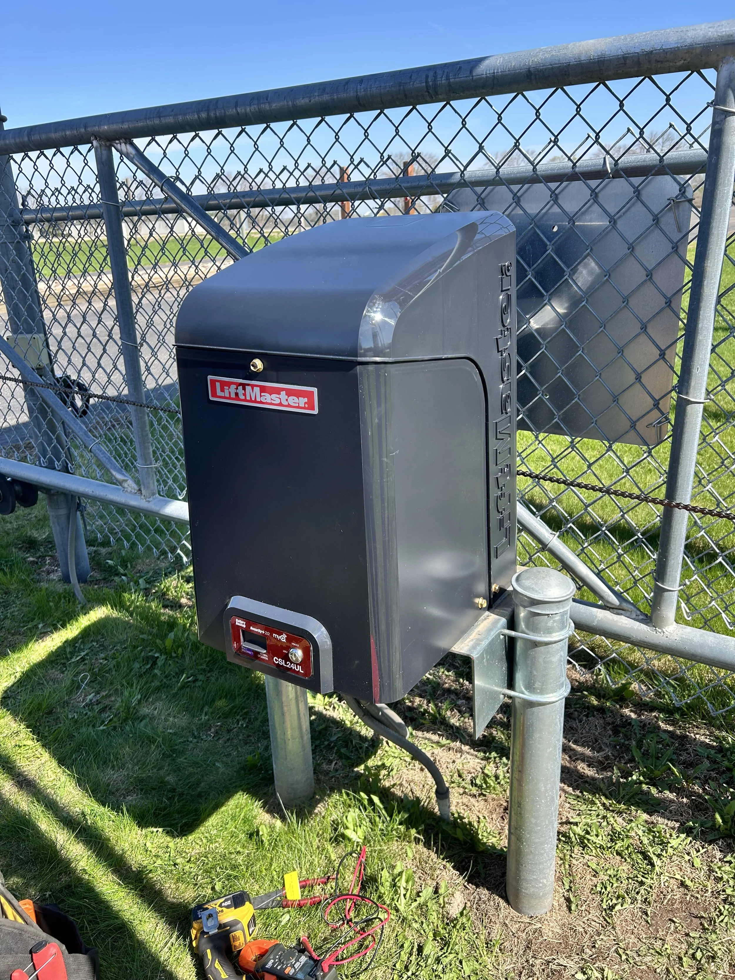 A substation with electronic equipment installed on a metal pole near a chain-link fence, with various tools and wires on the ground nearby.
