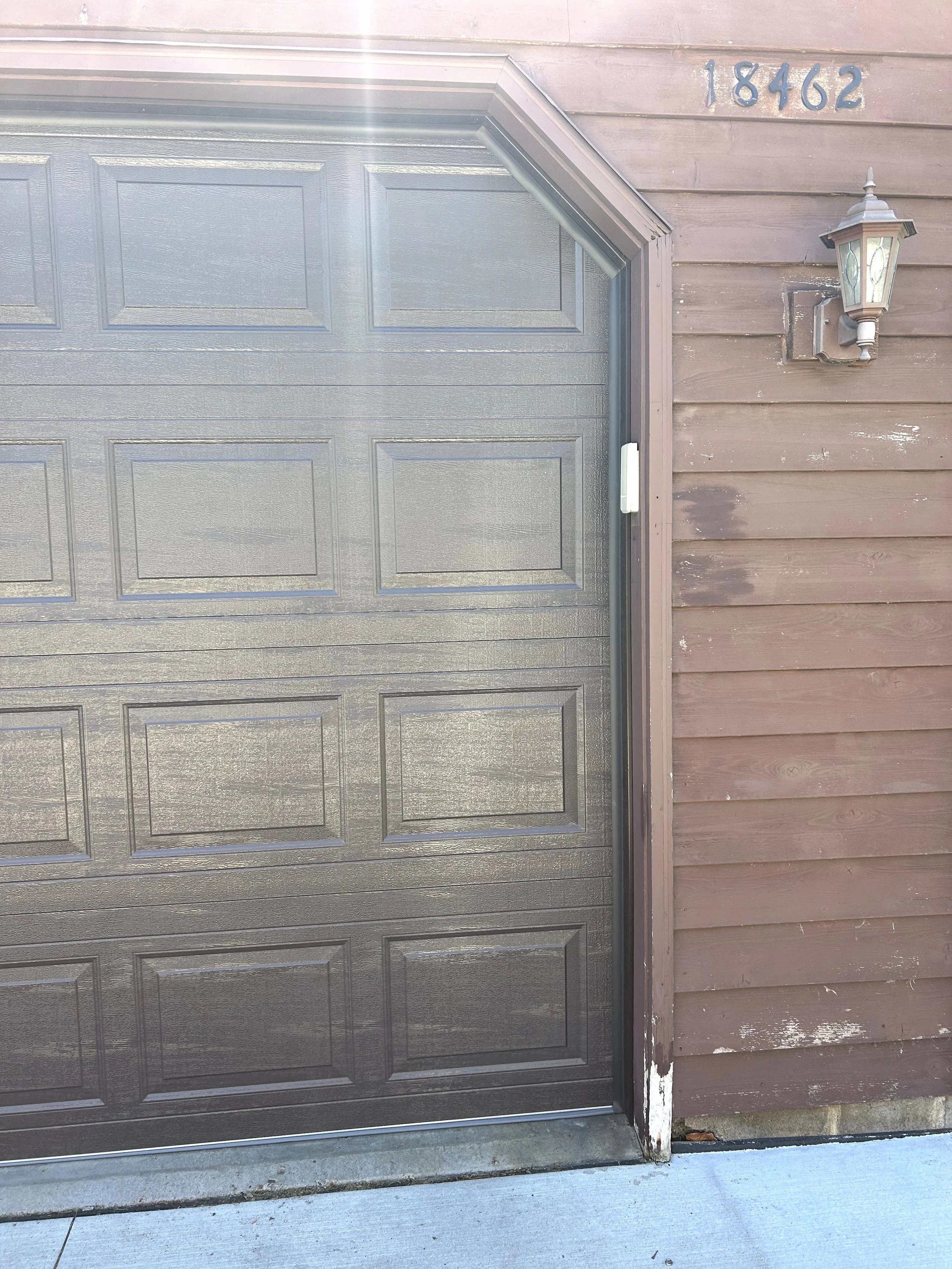 Close-up of a gray garage door with house number 18462 and an outdoor light fixture on a wooden wall.