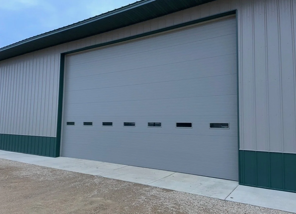 Large gray industrial building with a green trim and a roller door with small windows.
