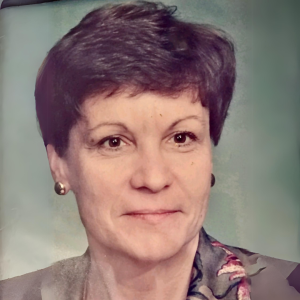 Close-up portrait of a middle-aged woman with short dark hair, wearing pearl earrings and a colorful scarf, against a muted background.