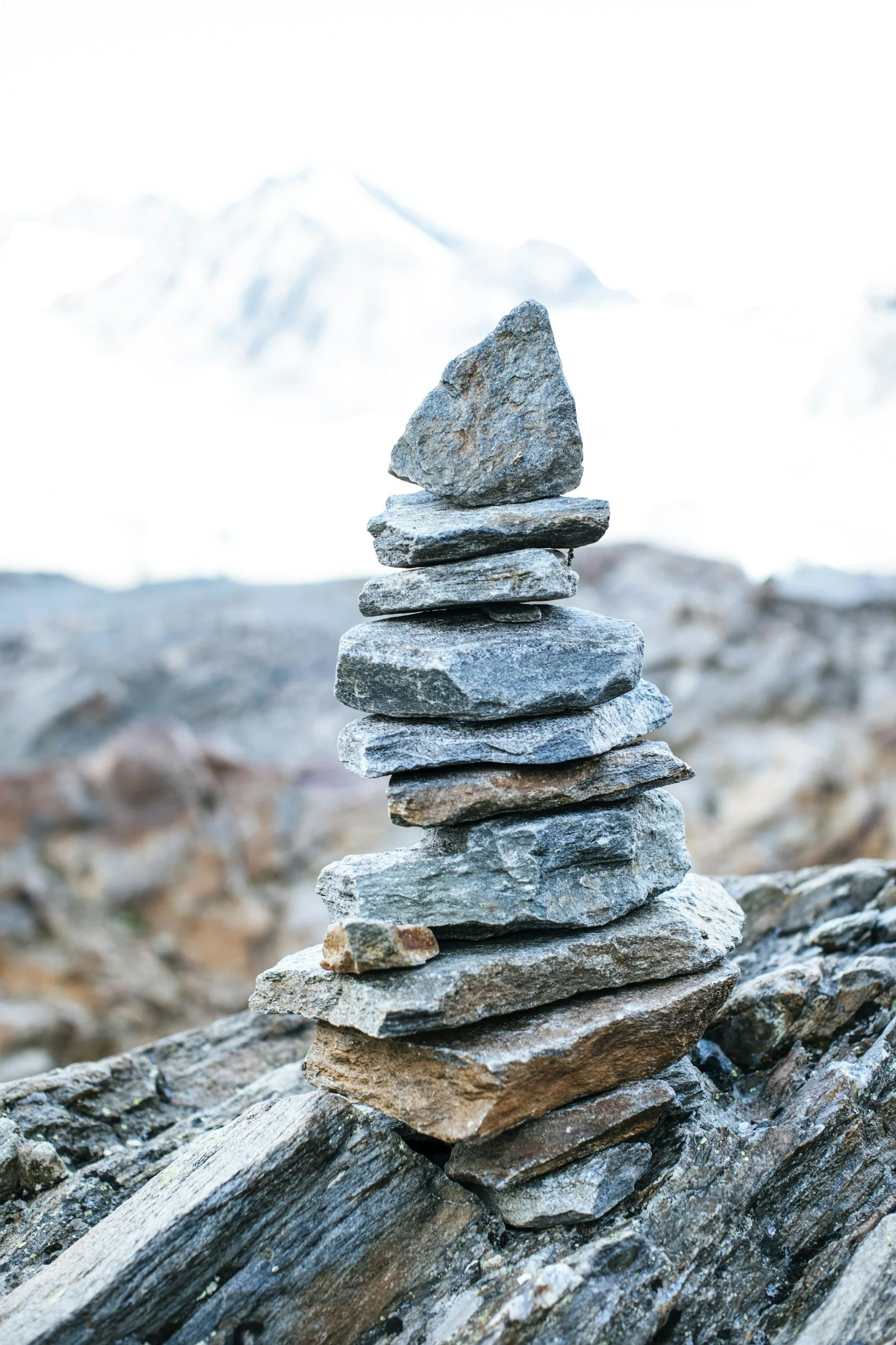 A stack of flat rocks balanced on a larger rock in a natural outdoor setting with snow-covered mountains in the background.