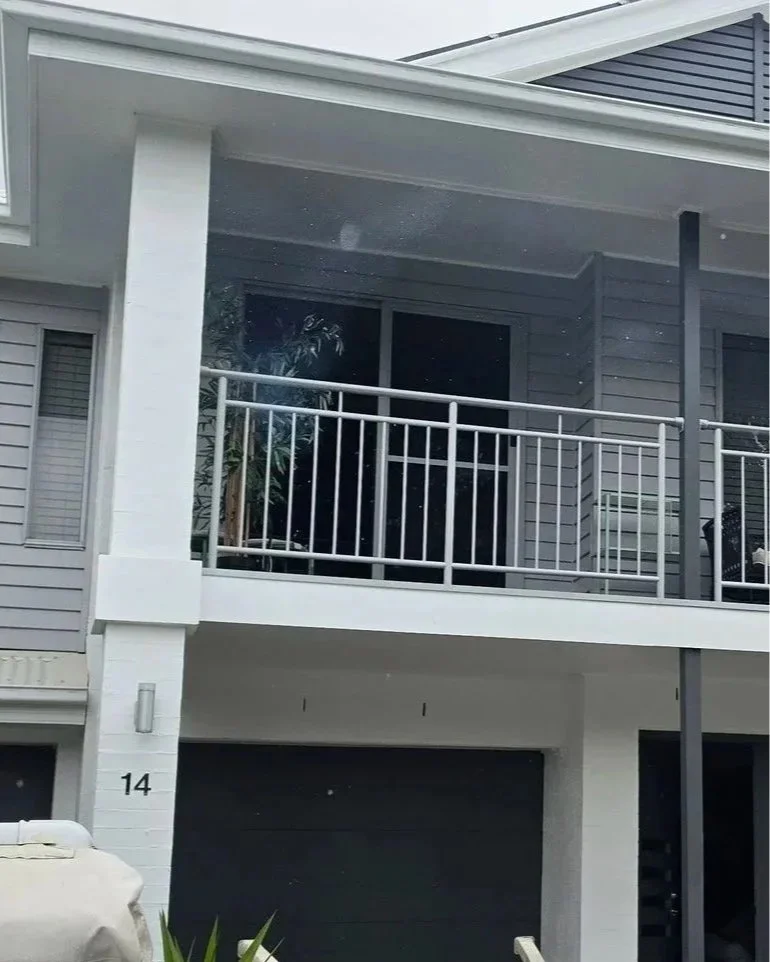 The exterior of a modern two-story house with gray siding, white accents, and metal balcony railings.