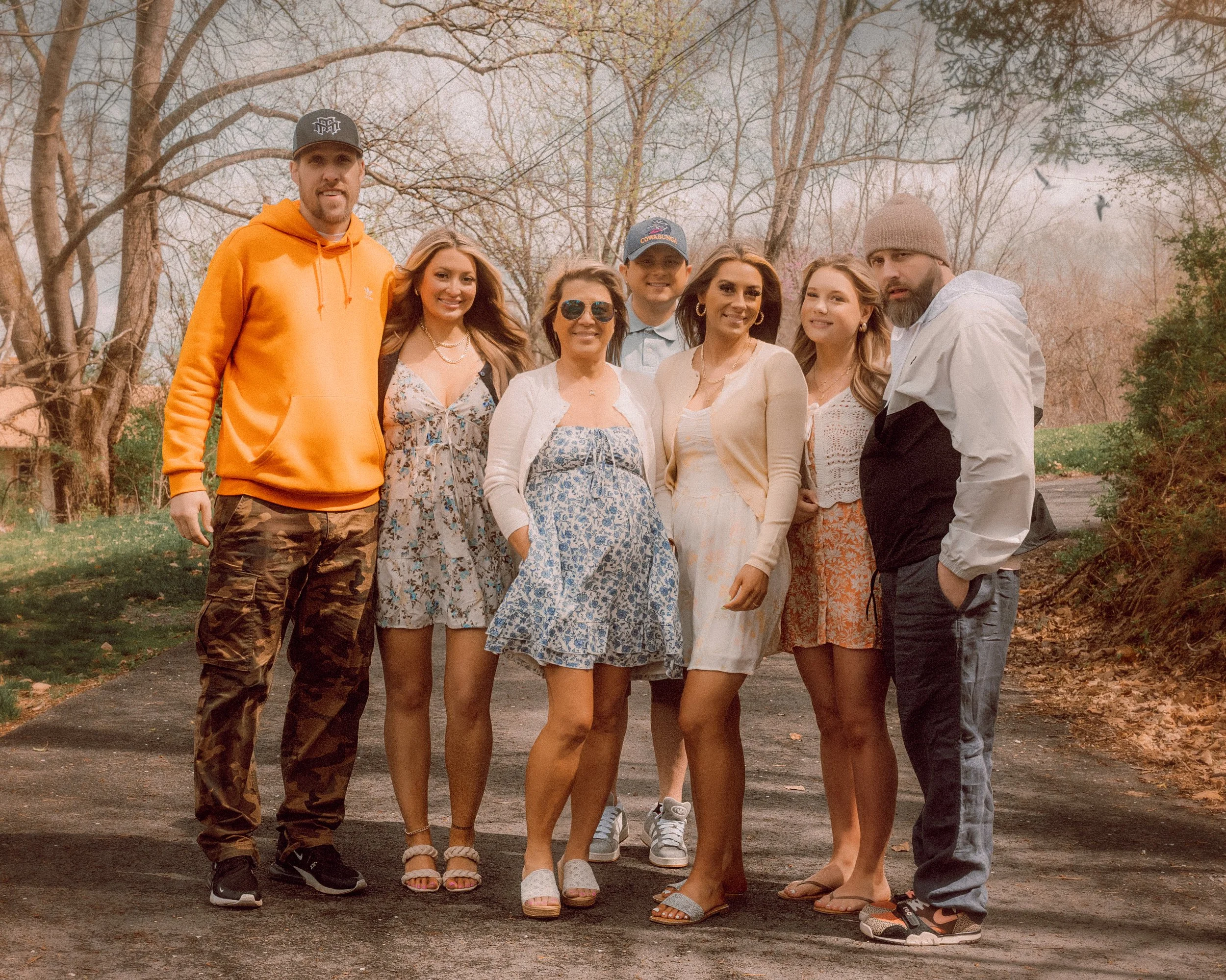 A group of eight people standing outdoors on a paved path, surrounded by trees with autumn leaves, posing for a photo with smiles.