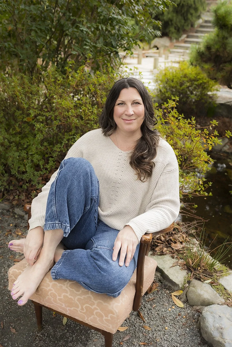 Woman sitting on a vintage armchair outdoors near a pond, surrounded by greenery.