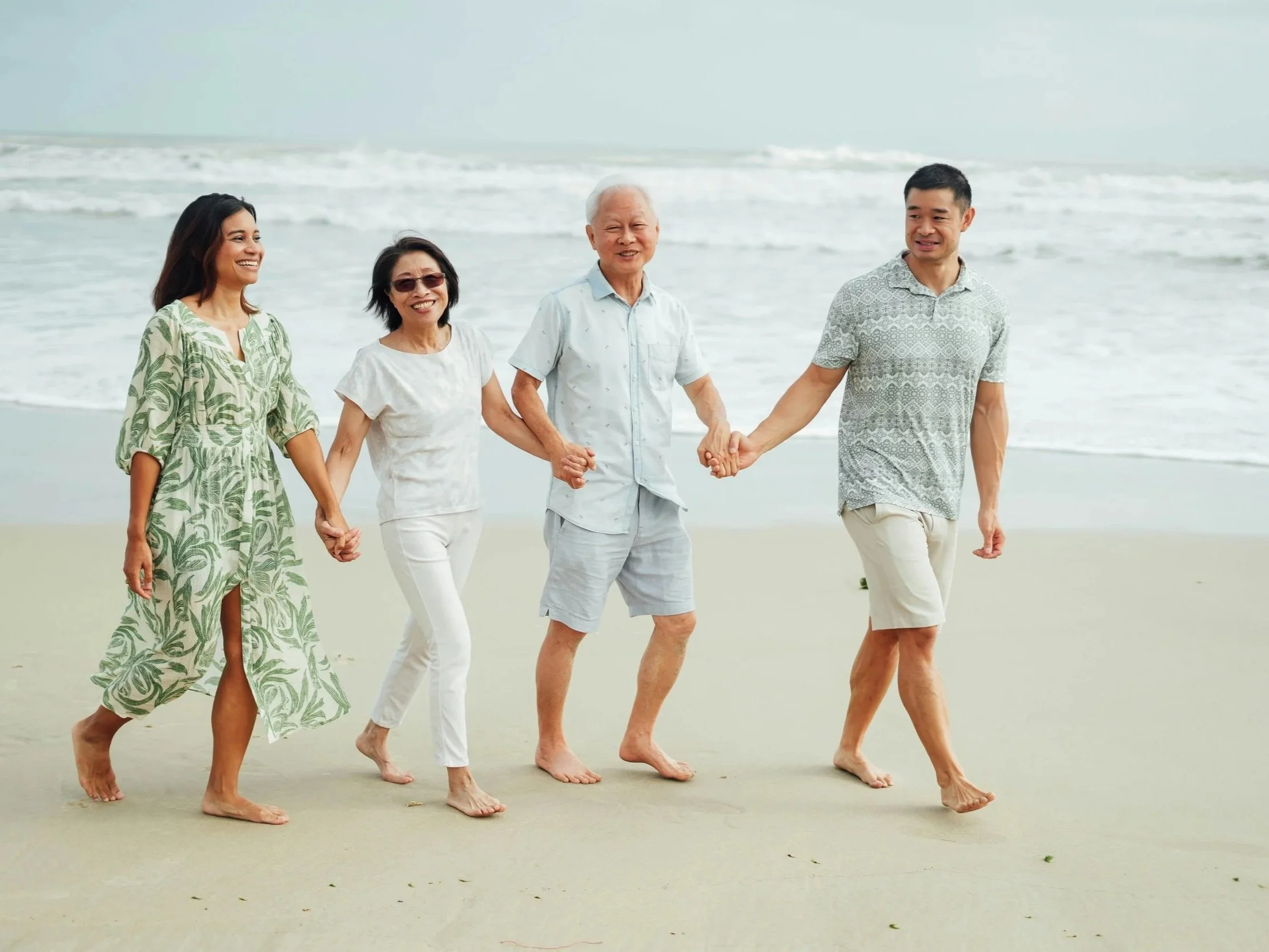 A family holding hands and walking along the beach with ocean waves in the background.