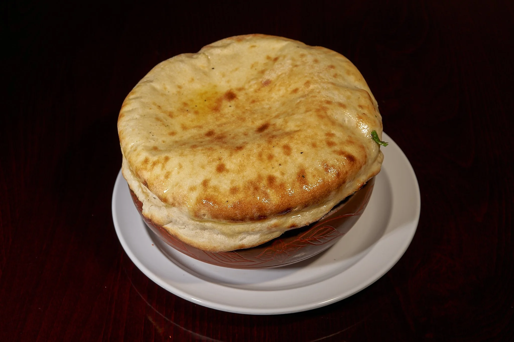 Bowl of Indian curry with a crispy naan bread on top, served on a white plate