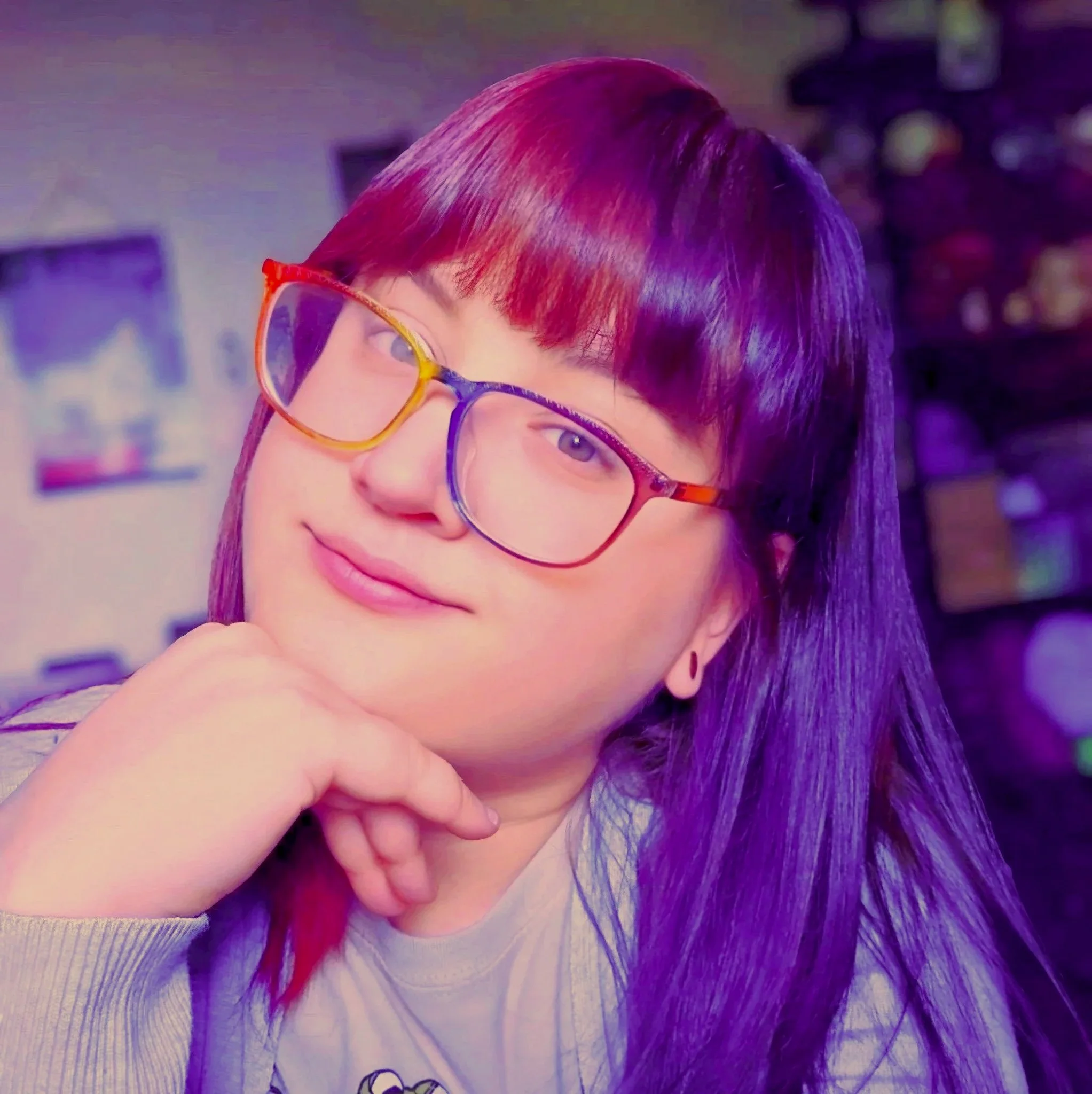 Close-up of a person with multicolored hair and colorful sunglasses, smiling slightly, in an indoor setting.