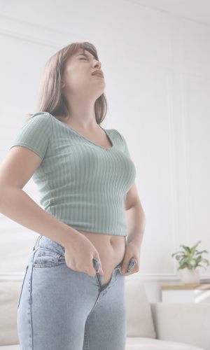 Young woman standing indoors with a pained expression, holding her stomach.