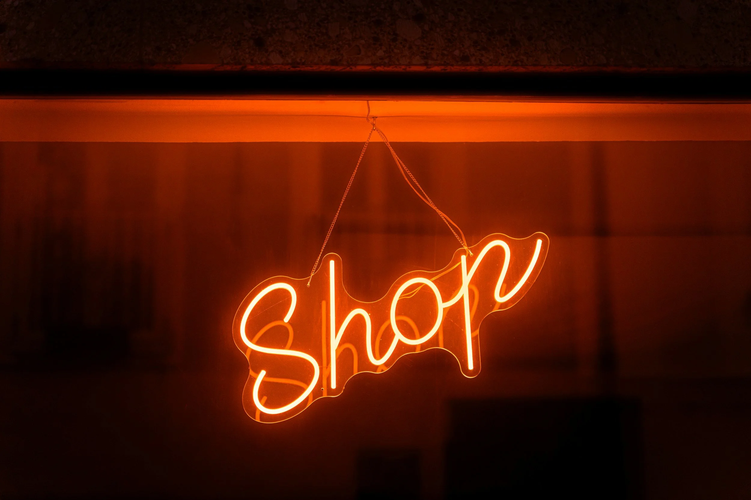 A neon sign with the word "shop" in bright orange, hanging from a chain against a dark background.
