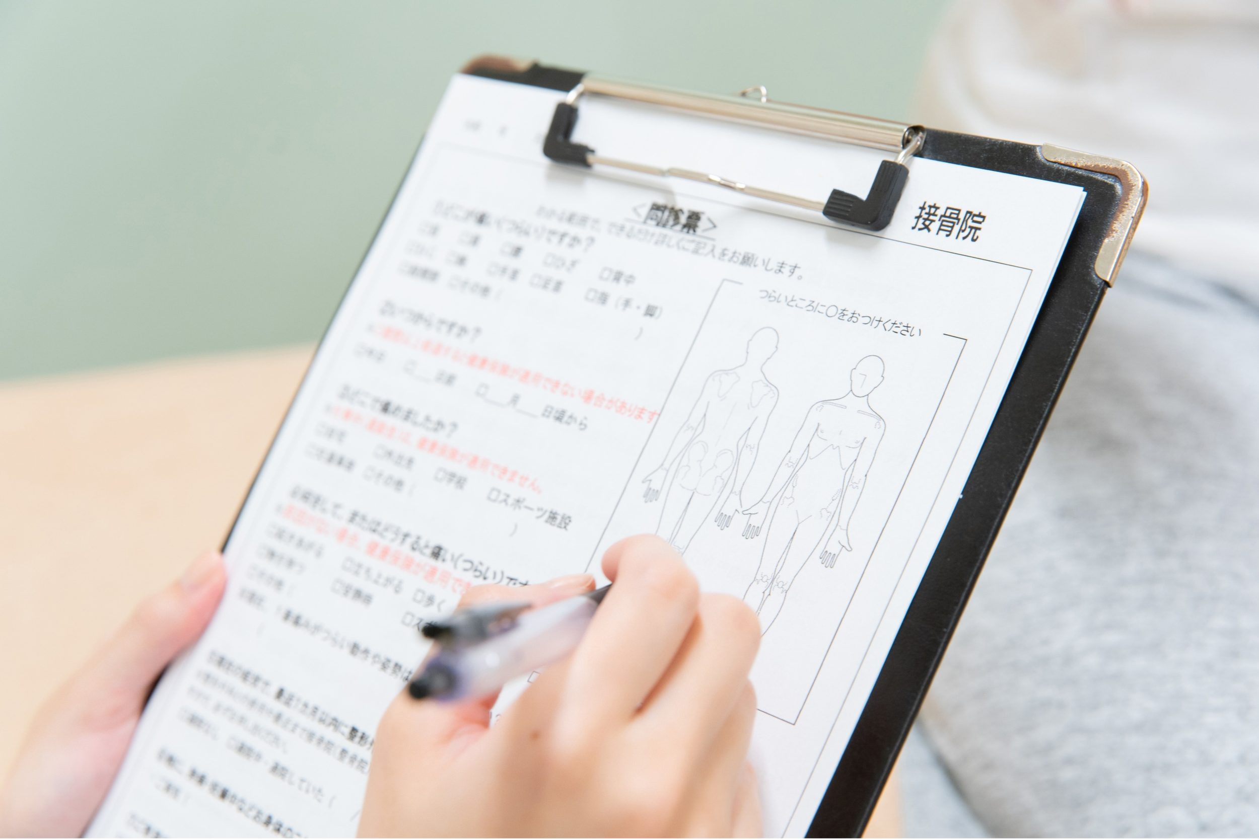 A person is holding a clipboard with a medical or anatomical form printed on it, which includes diagrams of the human body. The person is writing with a pen.