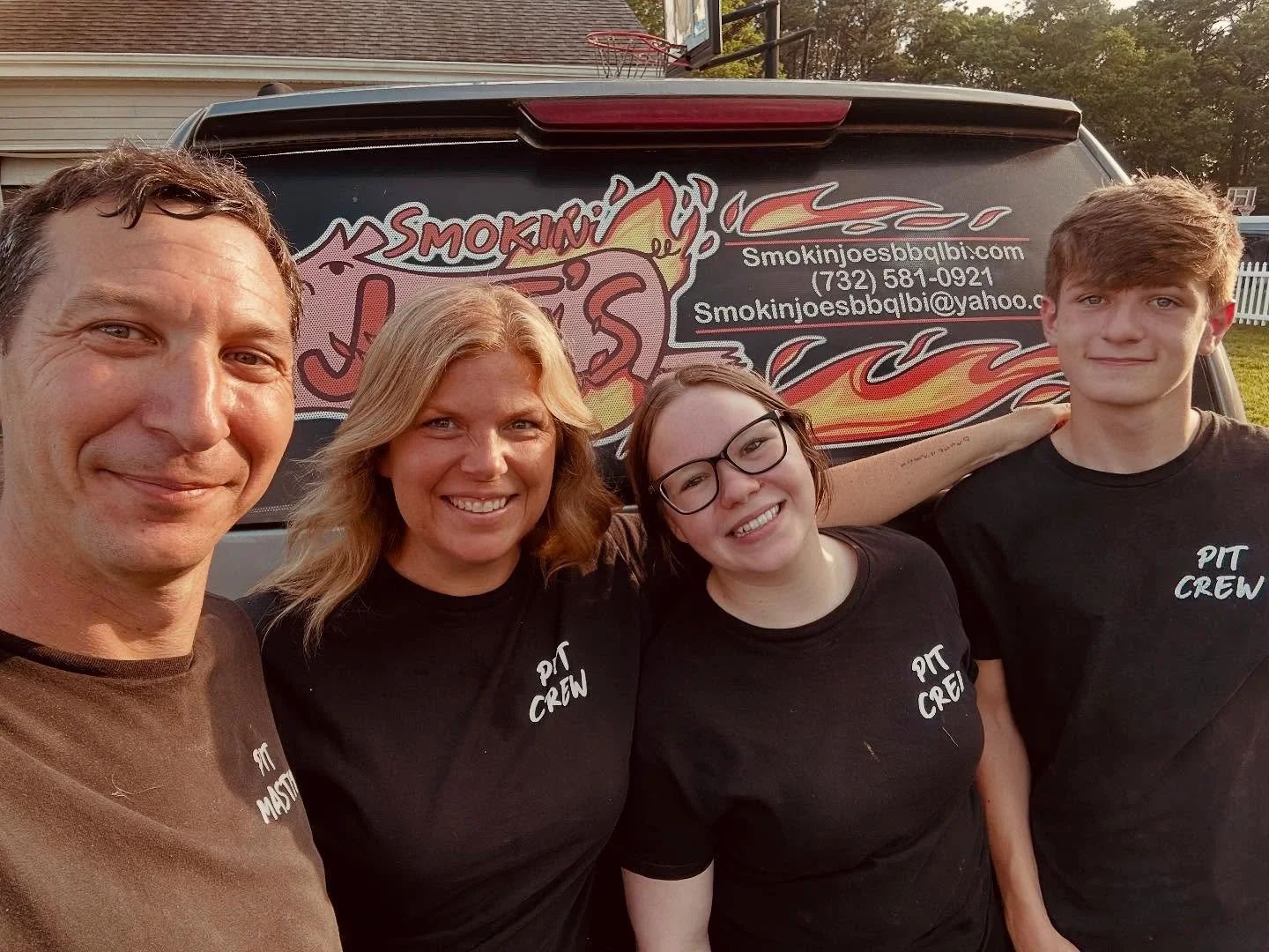 A group of four people taking a selfie in front of a food truck with a flaming pig logo and website URL.