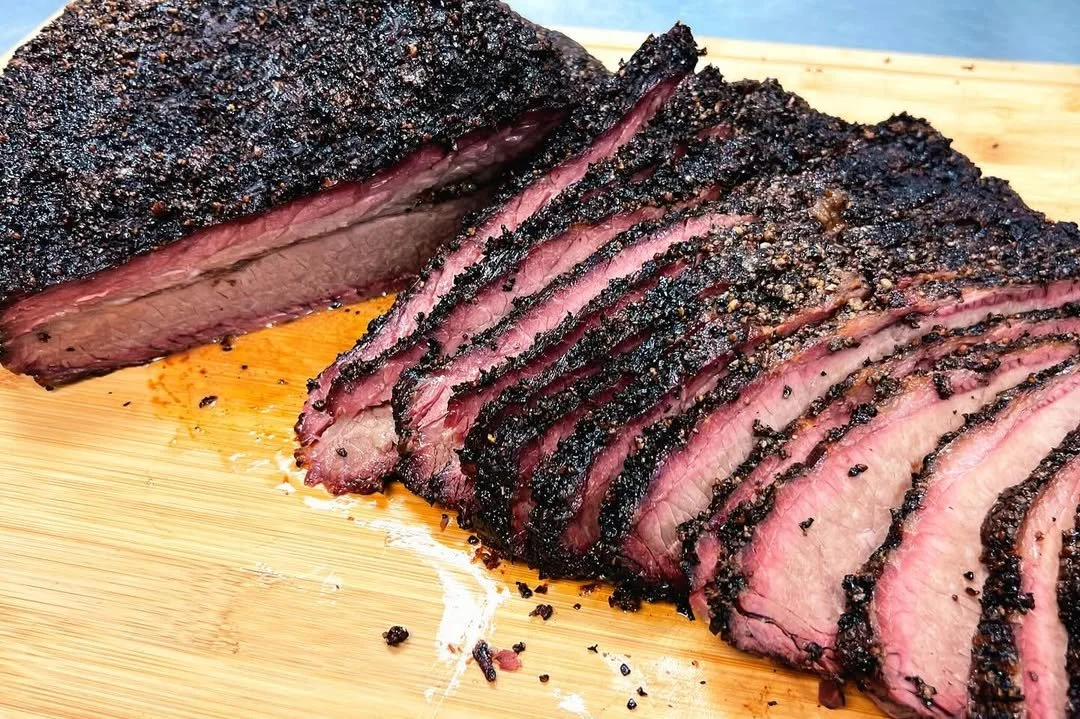 Sliced smoked beef brisket with a dark, peppery crust on a wooden cutting board.