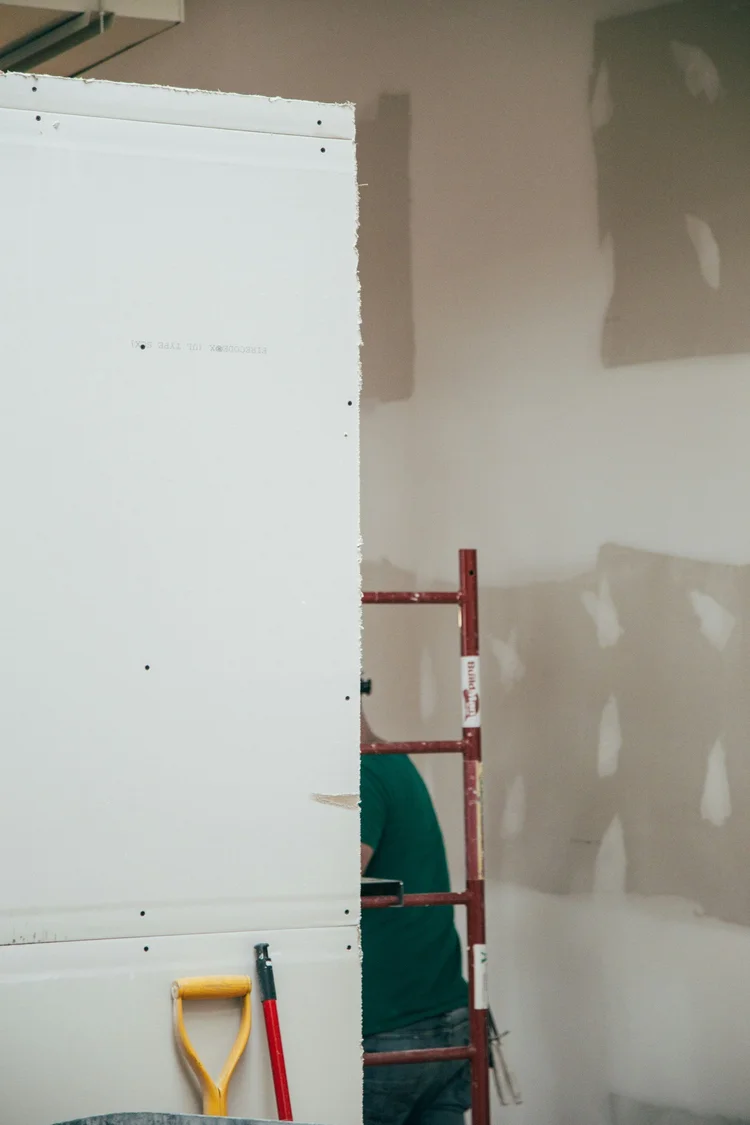 A sheet of drywall beside a wall with compound applied over repaired areas
