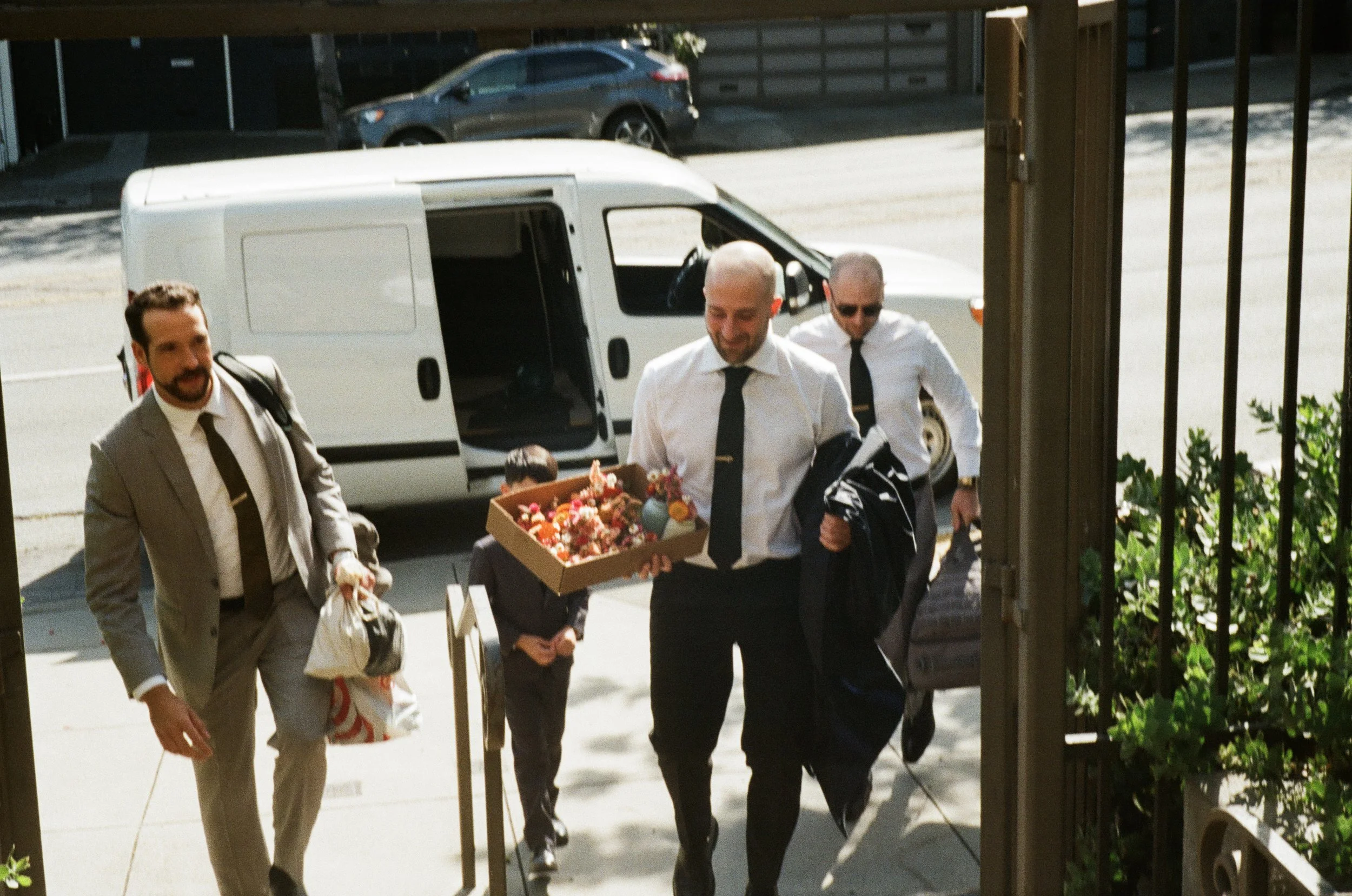 People carrying a box of flowers and wearing formal suits, walking out of a building.