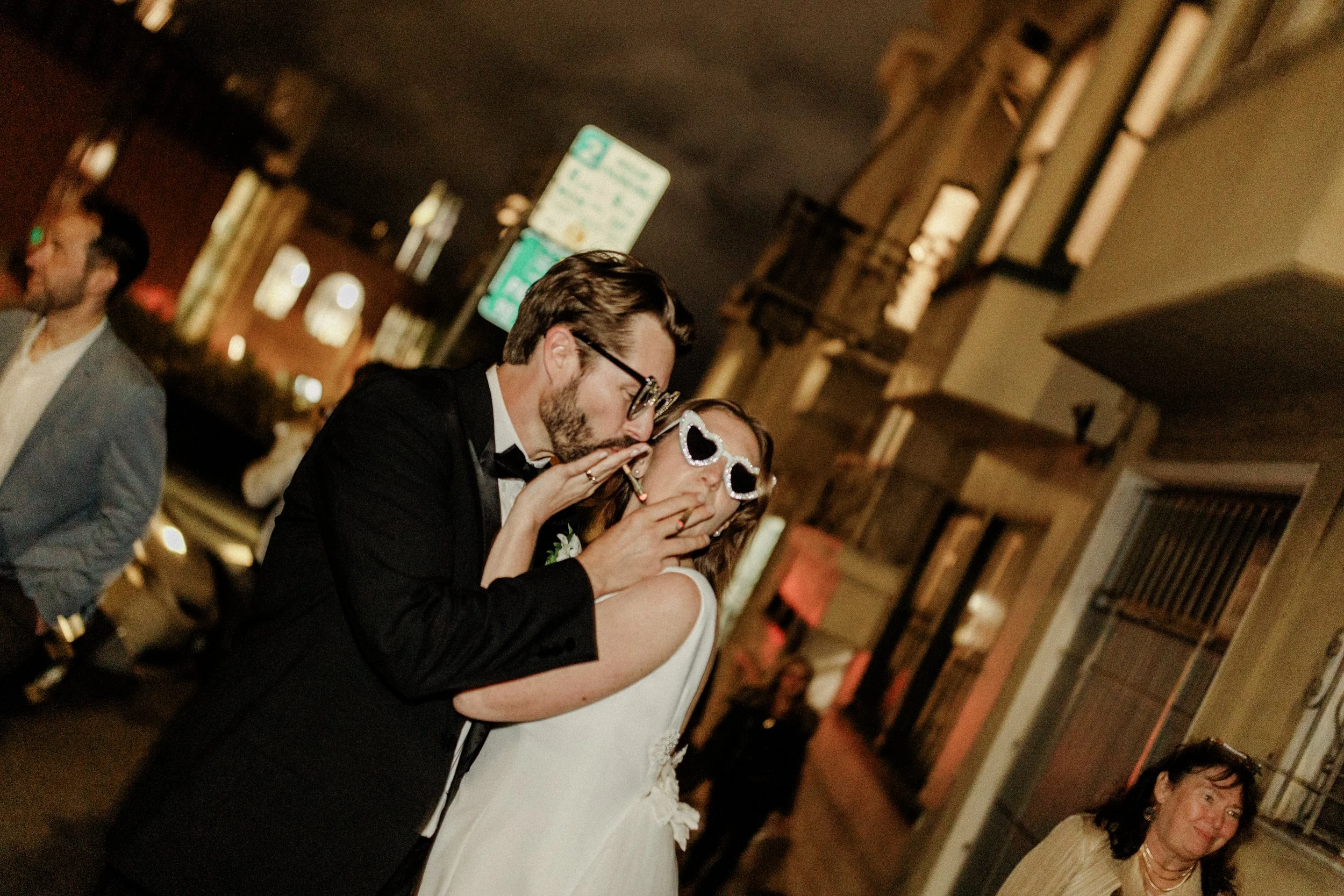 A bride and groom sharing a kiss at their wedding reception, with guests and a decorated venue in the background.