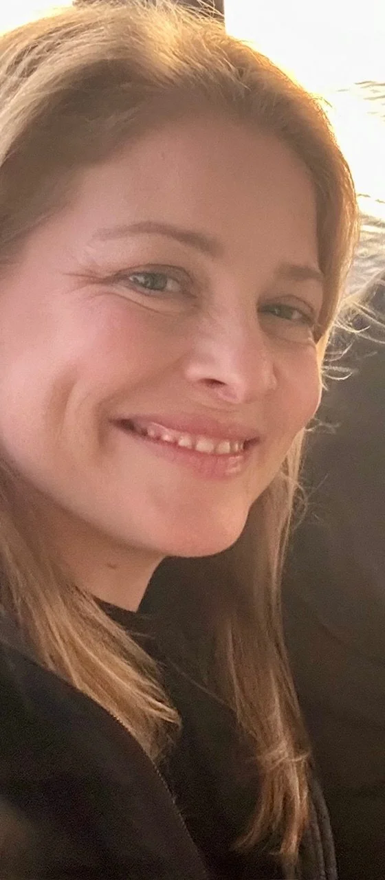 Close-up photo of a smiling woman with light brown hair and light eyes, wearing a black top.