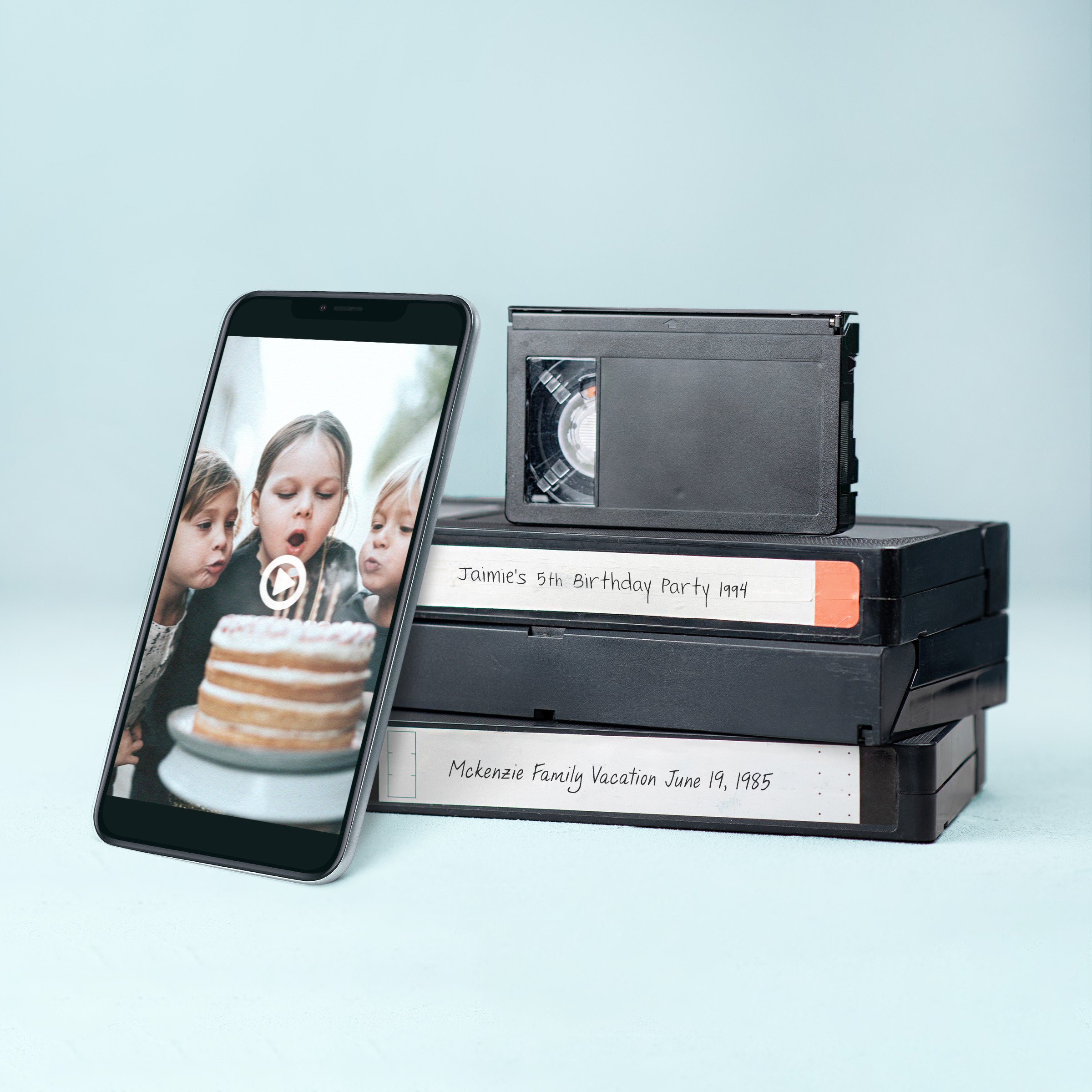 Image of VHS videos and a smart phone showing the video in digital form in the phone.