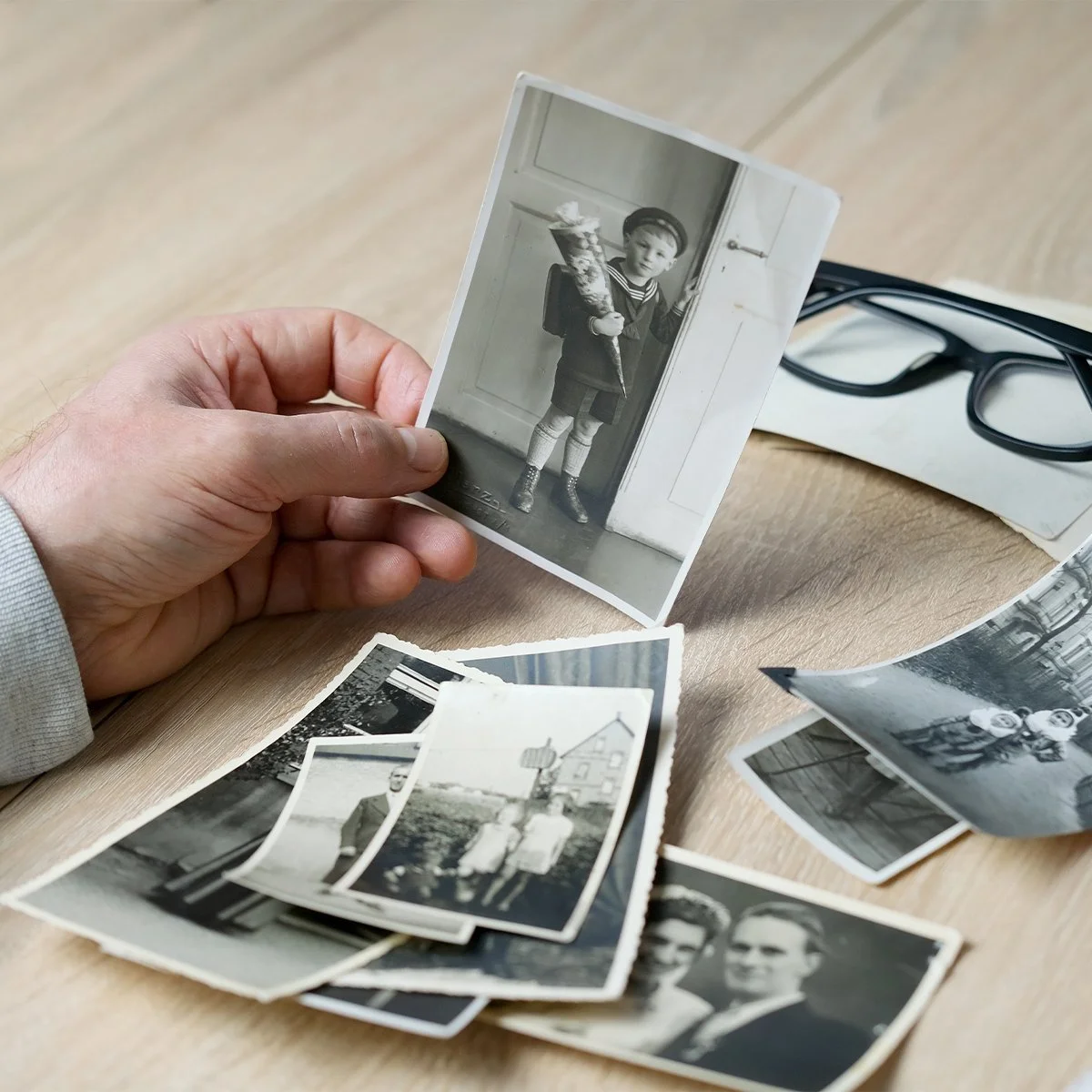 A hand holding old black & white print photos.