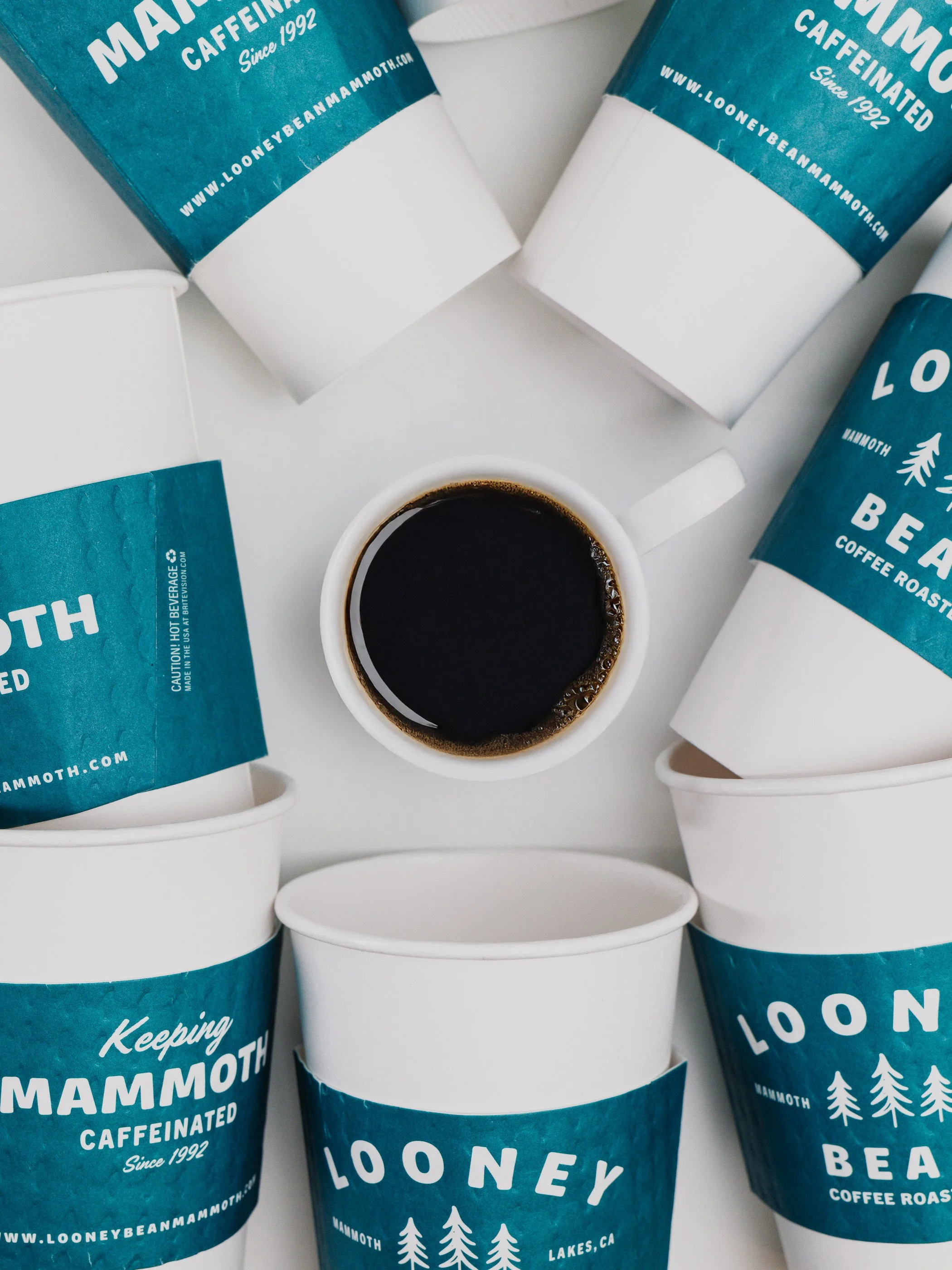 Top-down view of multiple coffee cups with blue sleeves and a cup of black coffee in the center.