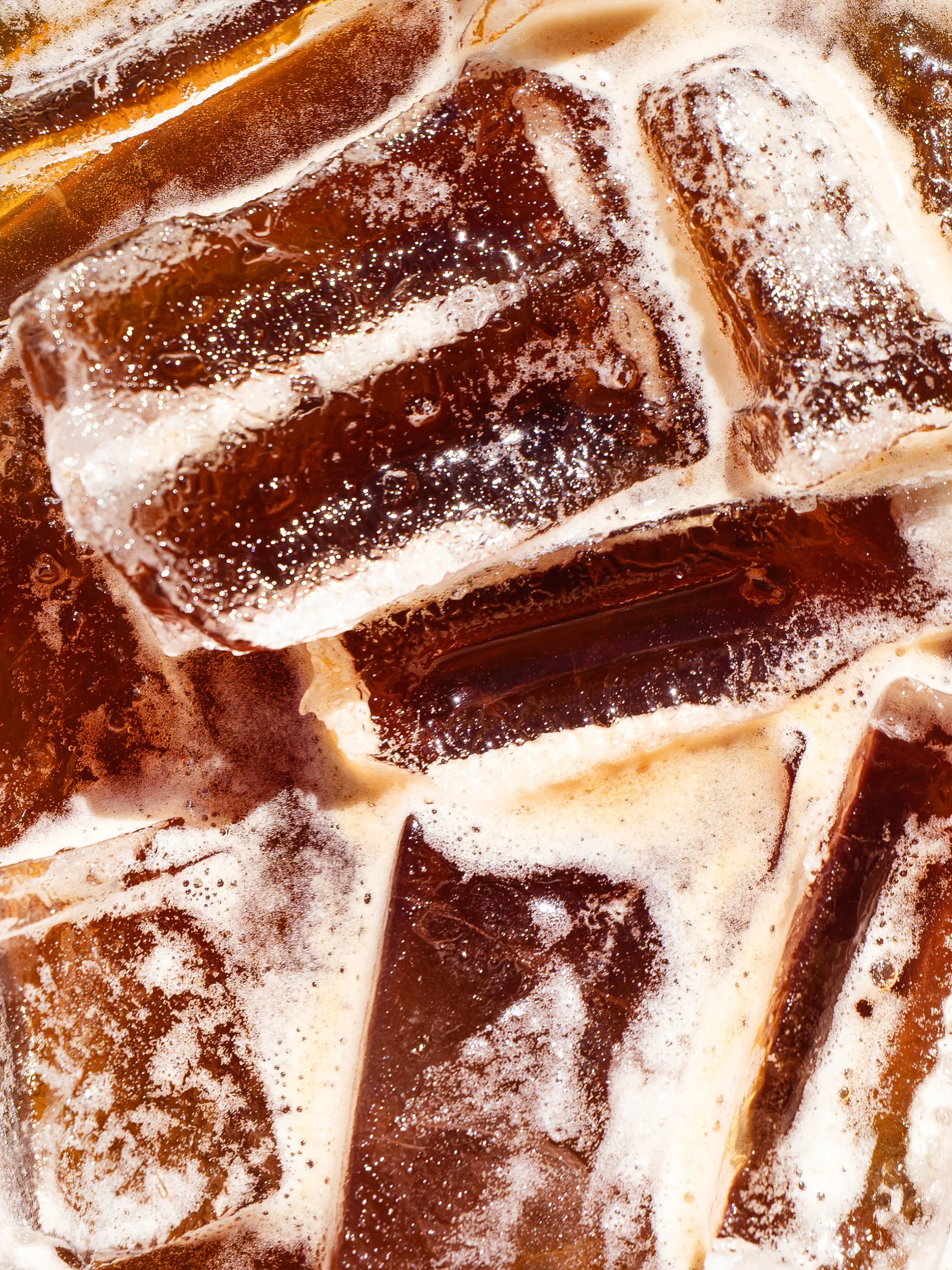 Close-up of ice cubes in a glass of cola with bubbles and foam.