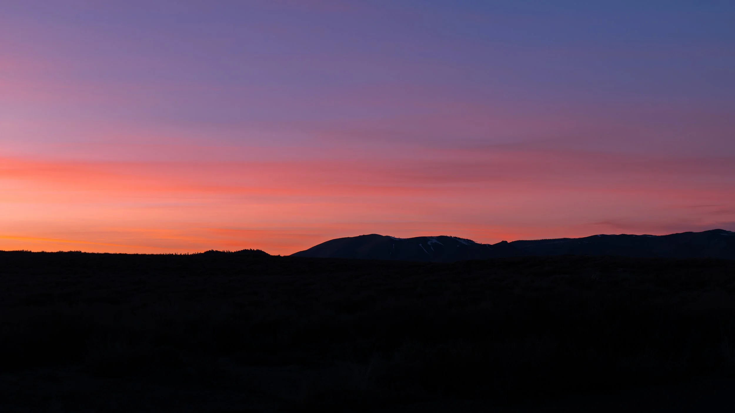 A landscape view of mountains at sunset with a colorful sky displaying shades of purple, pink, and orange.