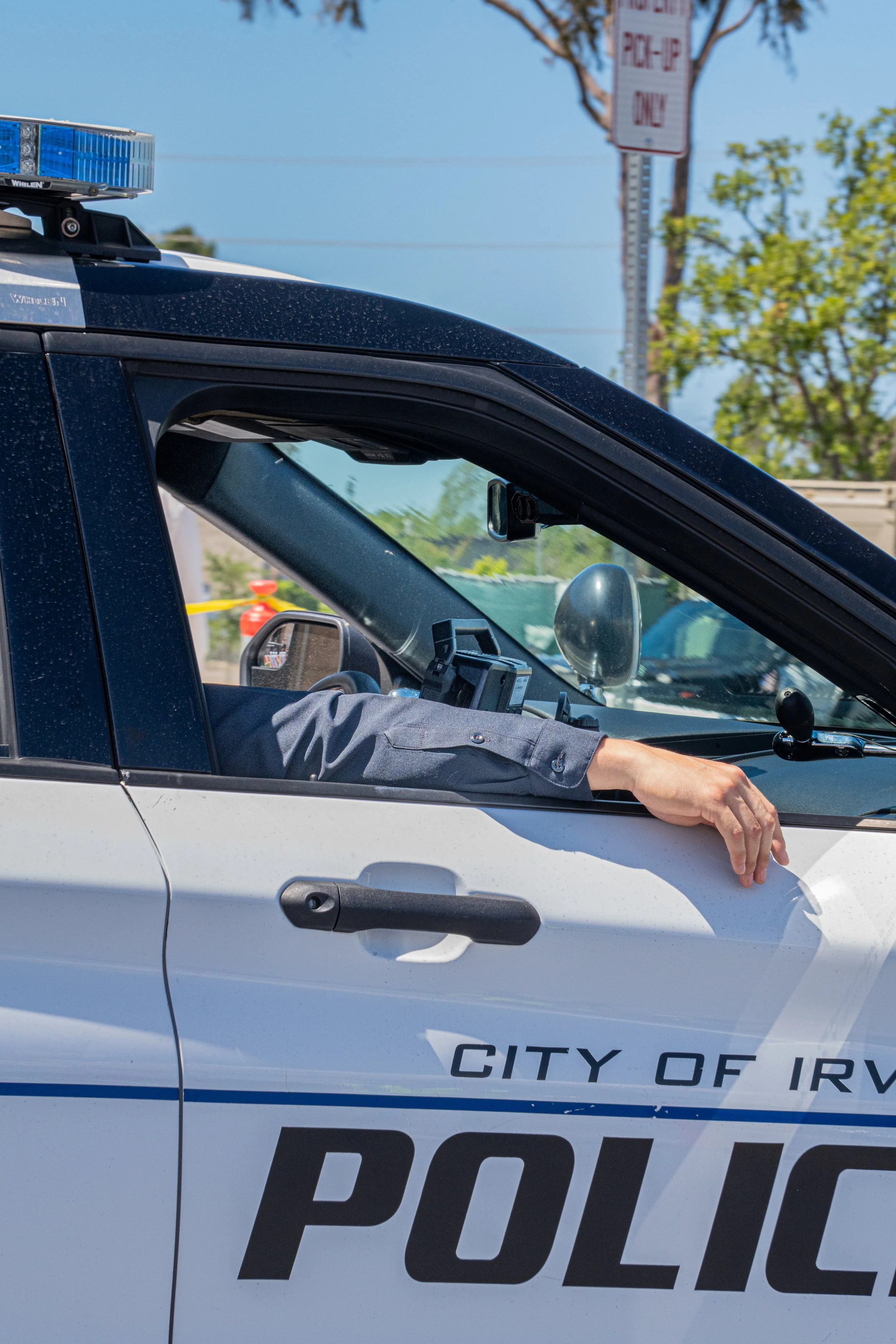 Close-up of a police car with the city of Irvine readable on the side, and an officer with an arm resting out the window.