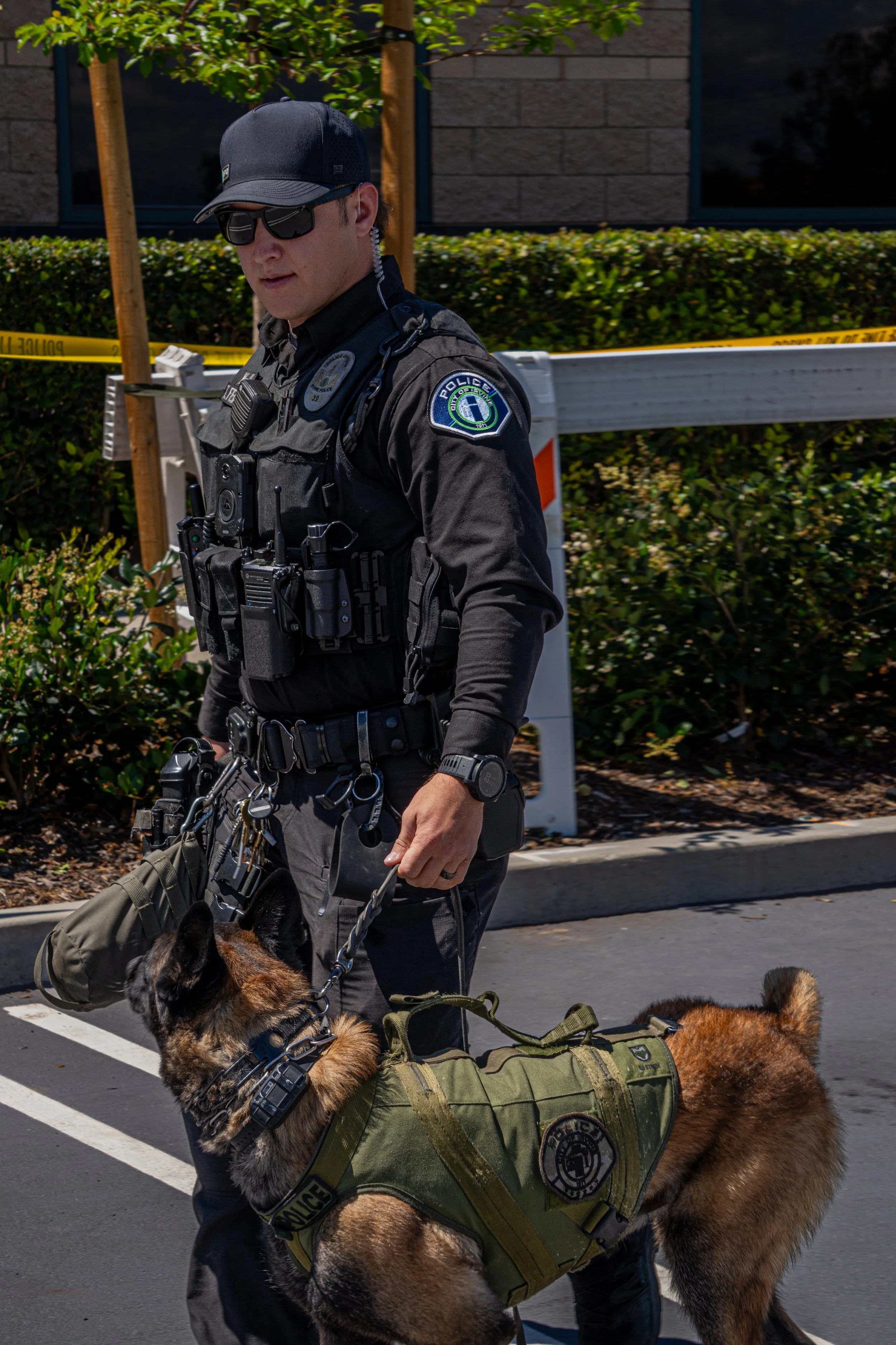 A police officer in uniform walking with a police dog on leashes in a parking lot.