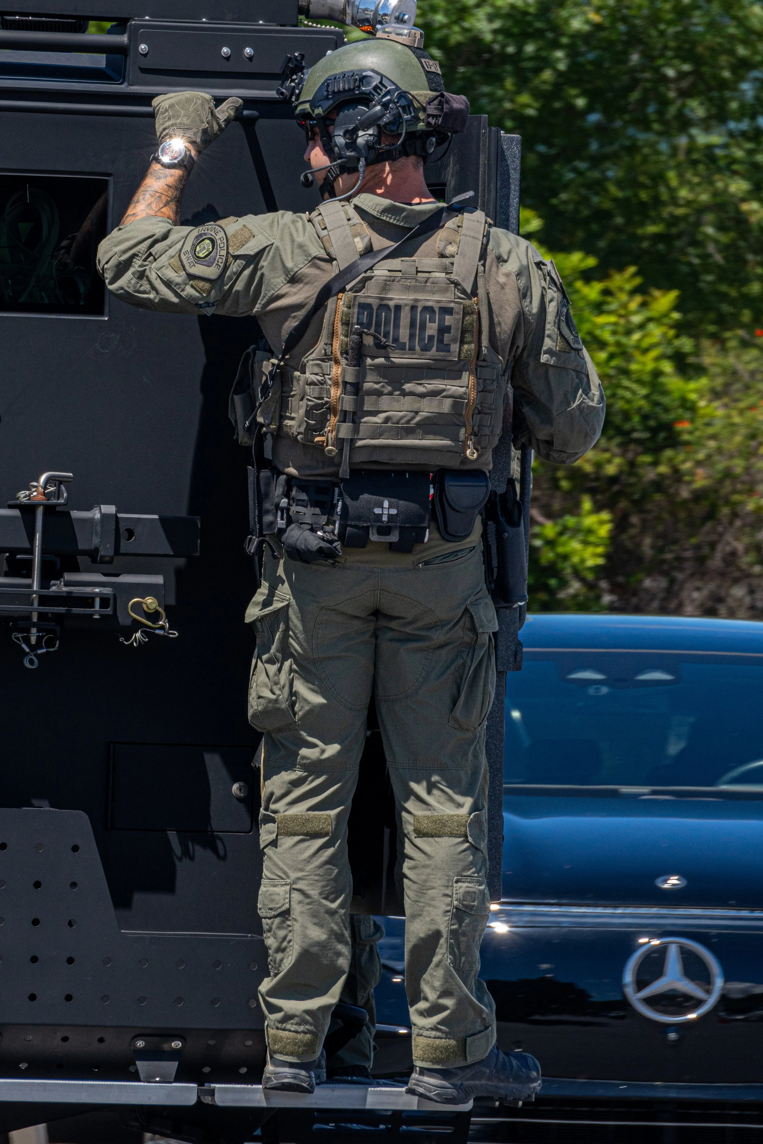 A police officer in tactical gear standing next to a police vehicle during daytime.