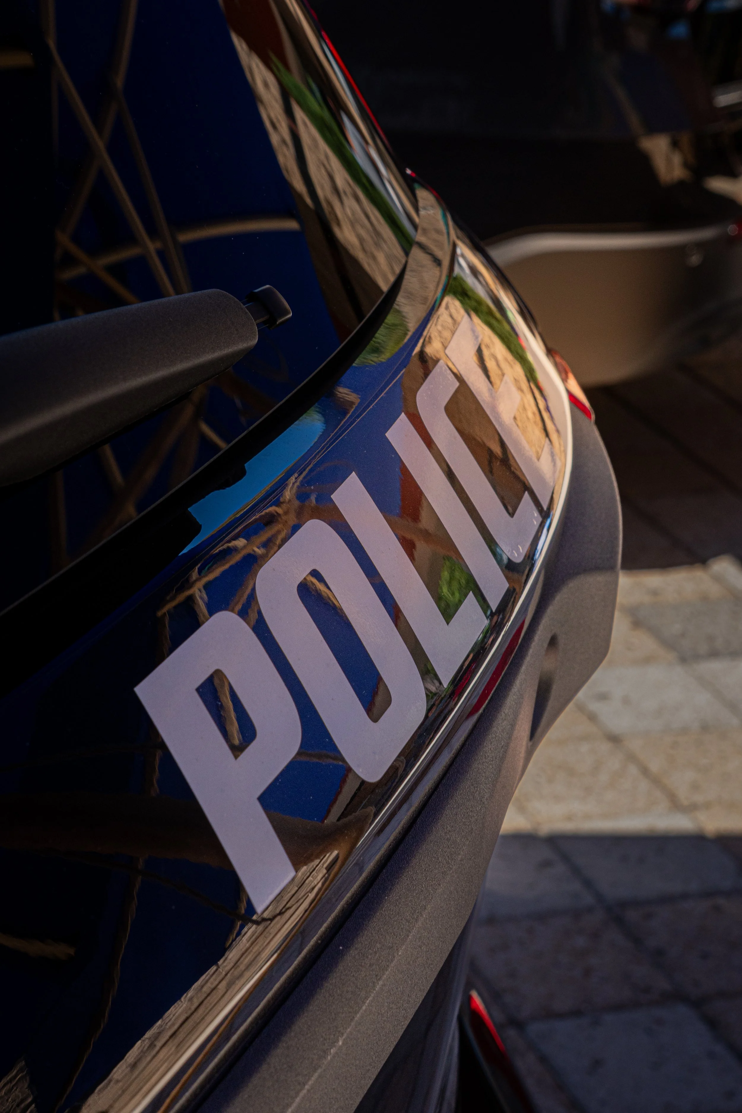 Close-up of a police car with the word 'POLICE' on the hood, reflected sunlight, and part of the windshield visible.