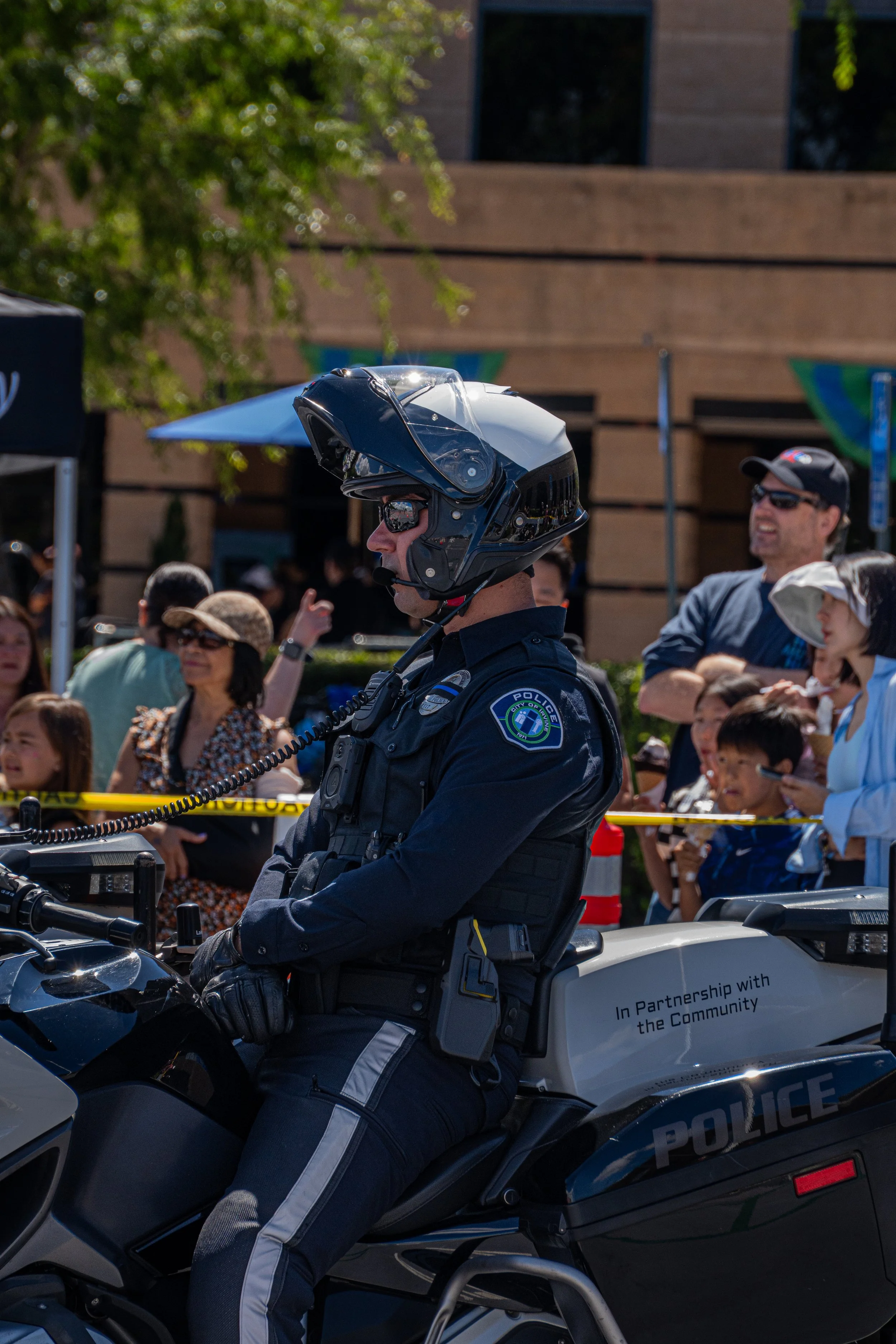 A police officer in uniform and helmet riding a motorcycle during a public event, surrounded by a crowd of people.