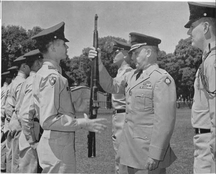Military personnel participating in a formal ceremony outdoors, with a focus on a woman receiving a medal or award from a senior officer.