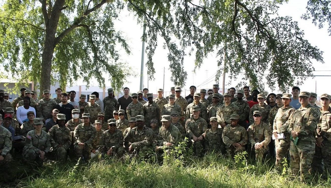 Group of soldiers and civilians outdoors under a large tree.