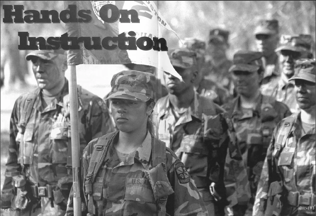 Black and white photo of a group of soldiers in uniform standing in formation, with one soldier in the front holding a sign that says "Hands On Instruction."