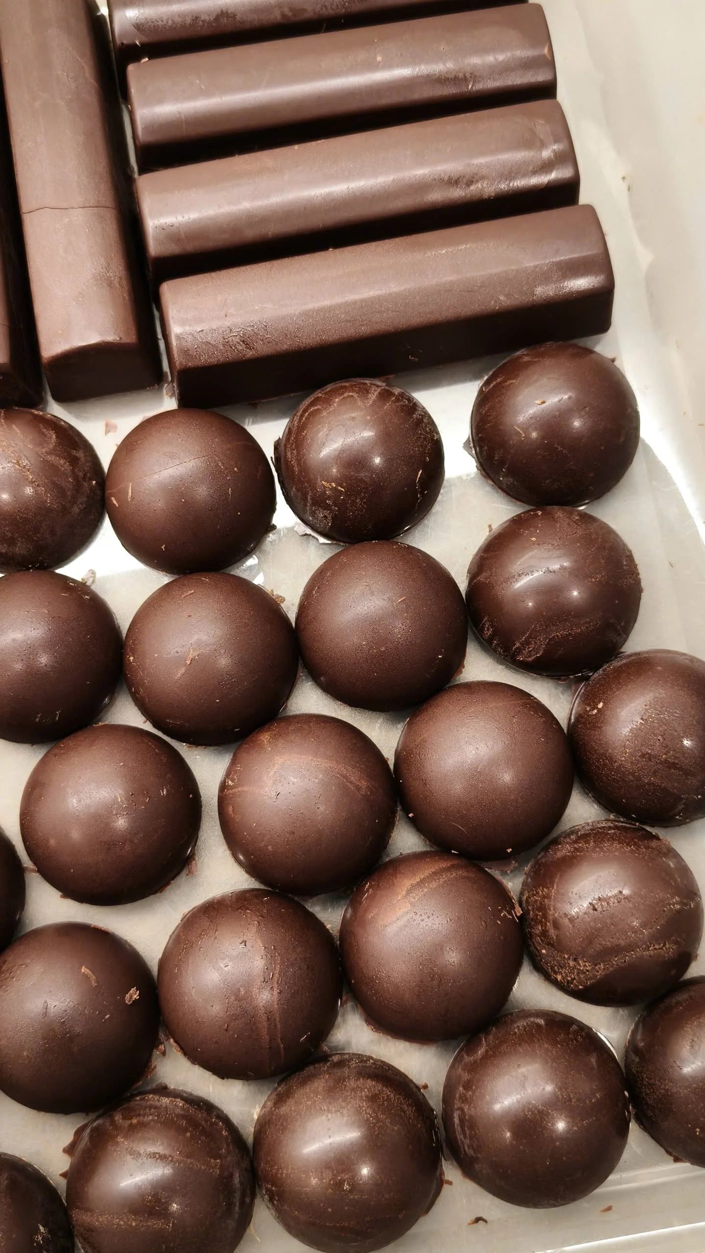 An assortment of dark chocolate confections including round truffles and rectangular chocolate bars.