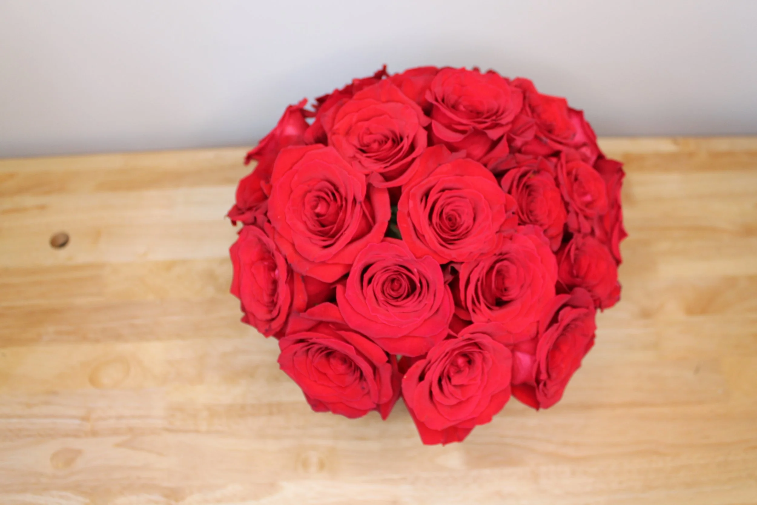 A bouquet of red roses arranged in a circular shape on a wooden surface.