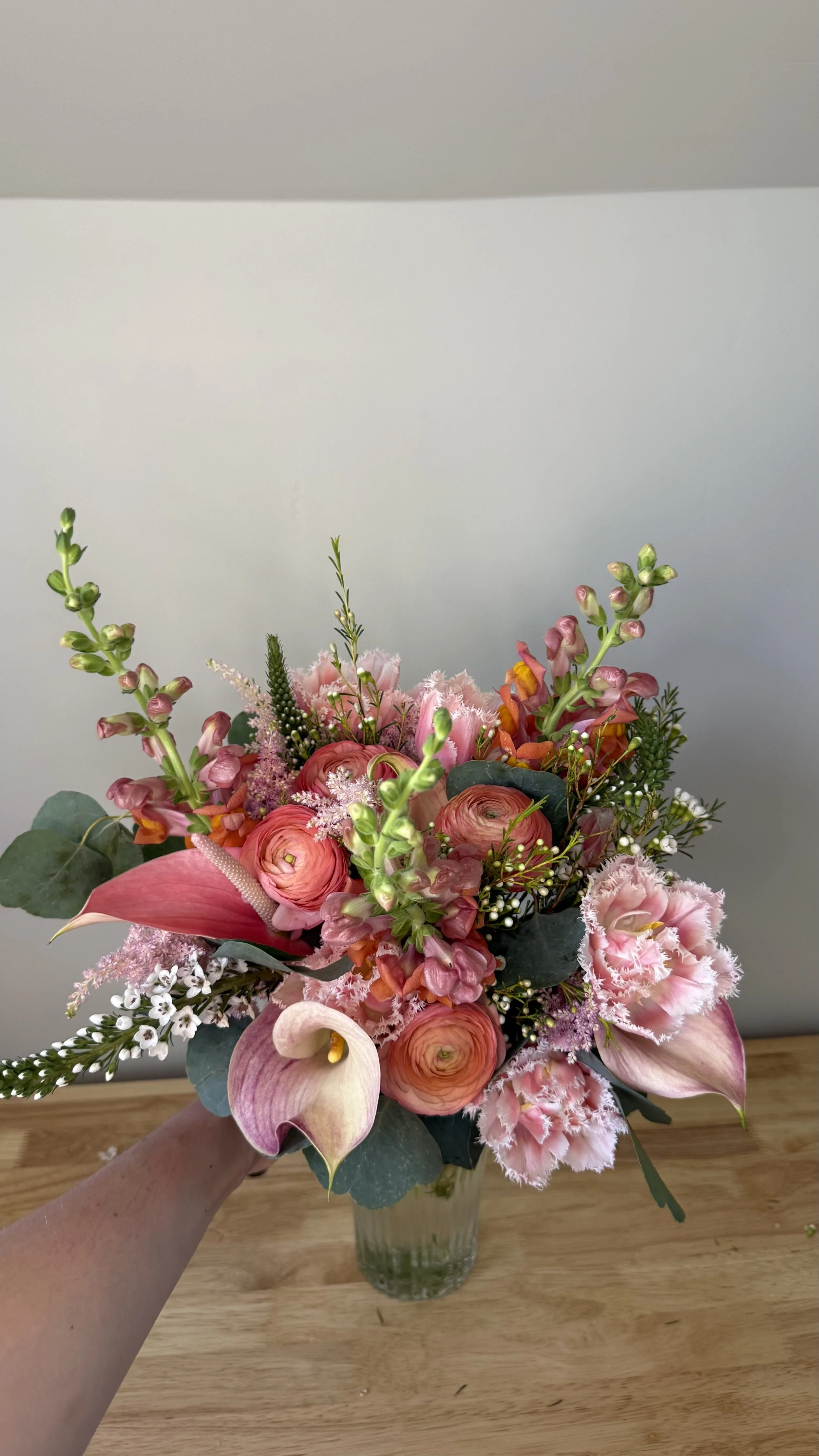 Colorful bouquet of pink, peach, and white flowers in a glass vase on a wooden table.