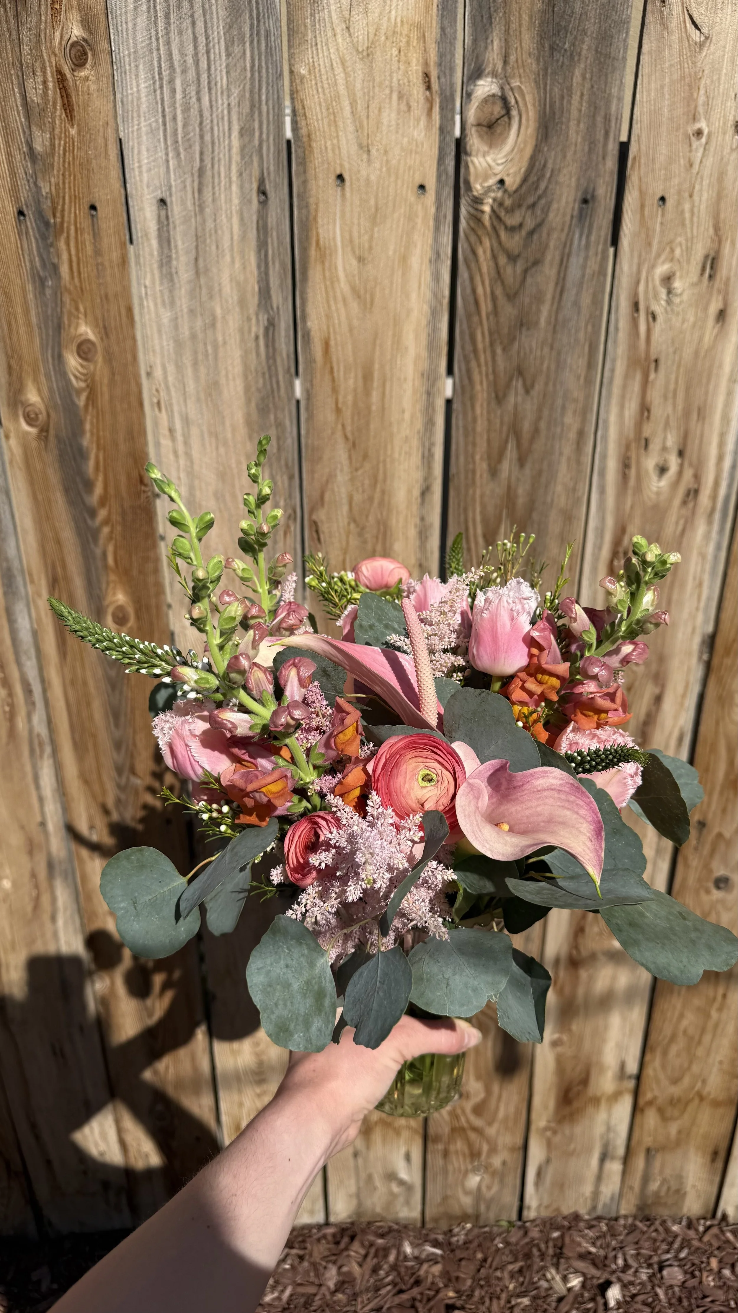 A person holding a bouquet of pink and purple flowers in front of a wooden fence.