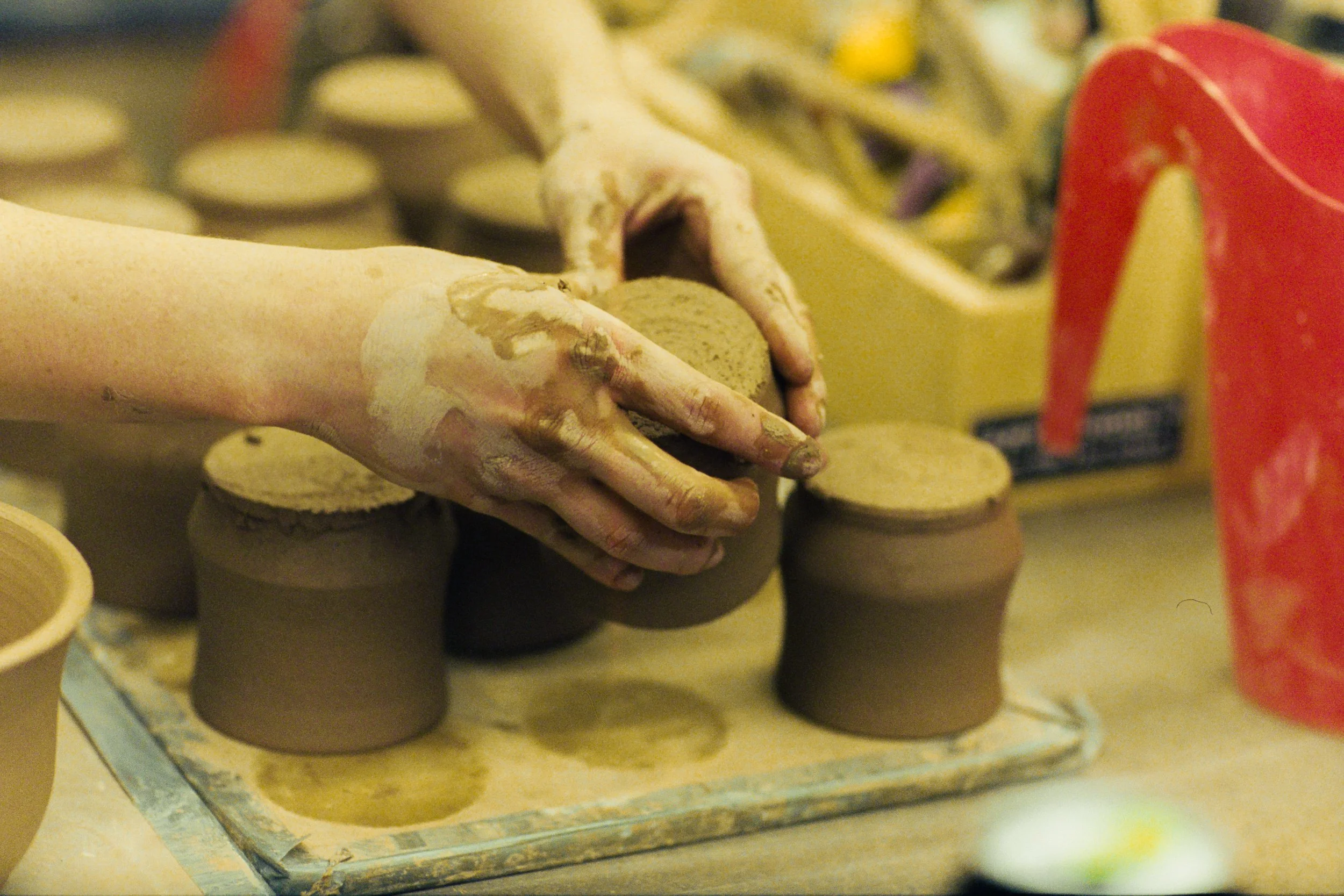 Close-up of a hand shaping pottery on a pottery wheel, with other ceramic pieces and tools in the background.